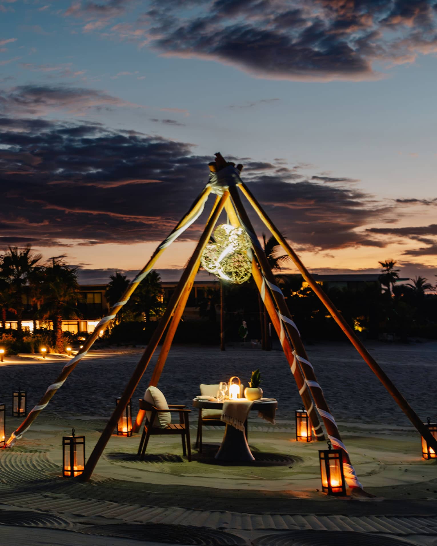 Outdoor tent with a chair and dining table, surrounded by lanterns on the ground in the evening.