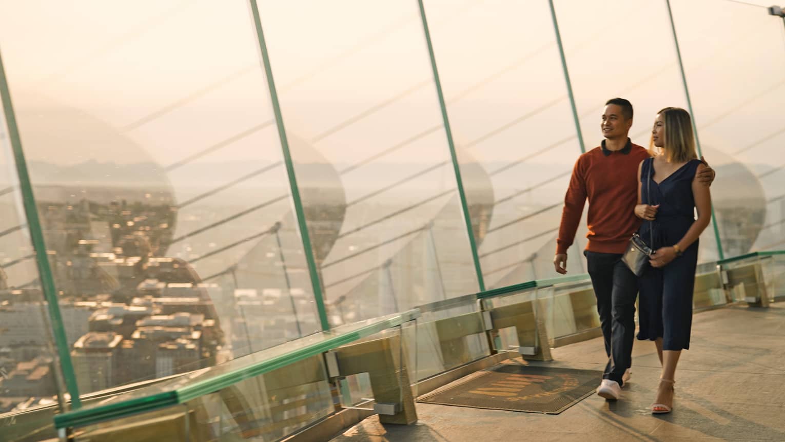 A man and woman walking in a tall building with glass walls looking out at a city.