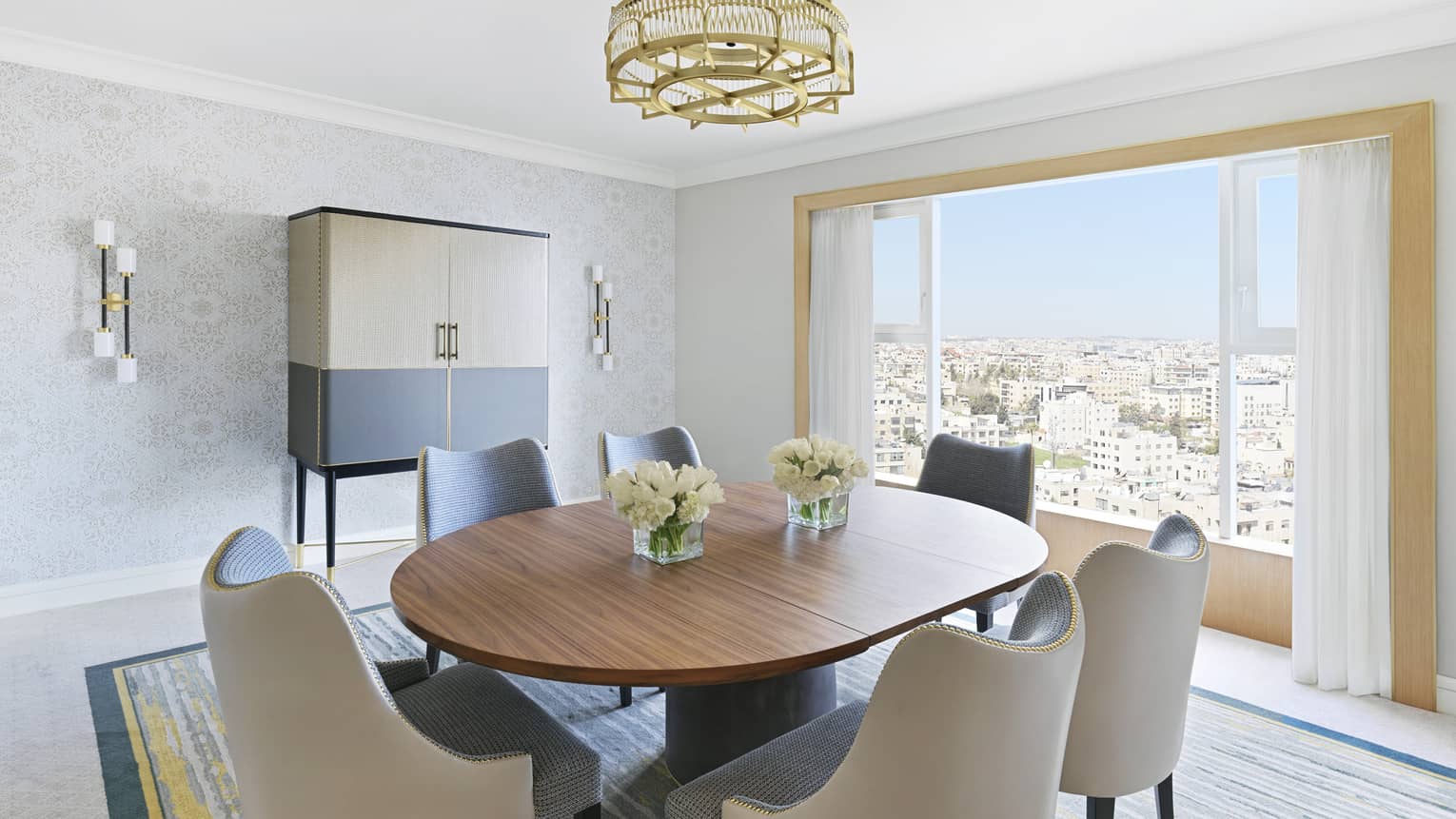 A brown table in the centre of a small room surrounded by plush white chairs. 