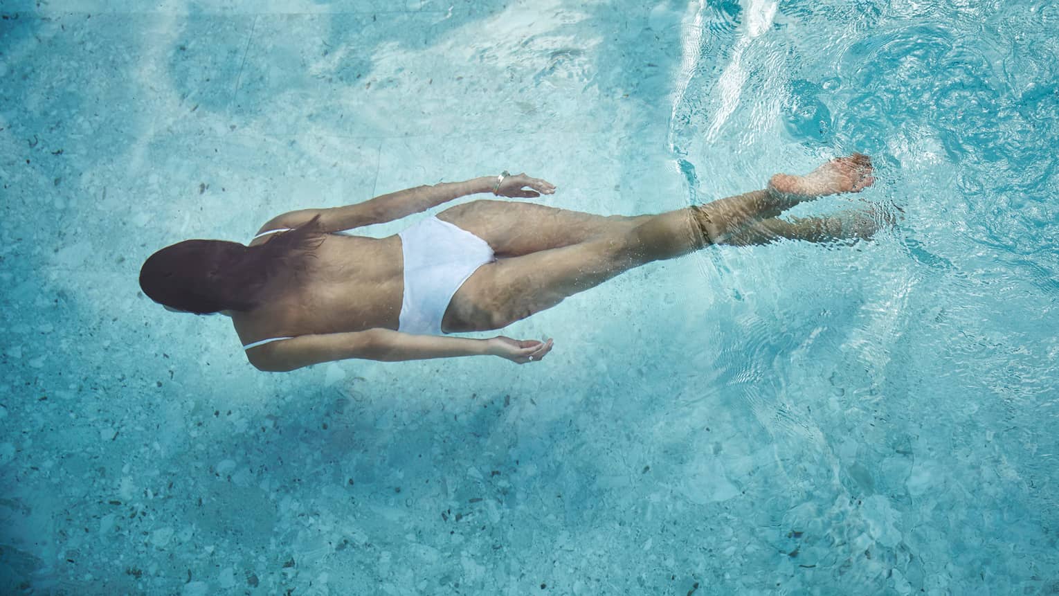 Woman in white swimsuit swimming underwater in blue pool