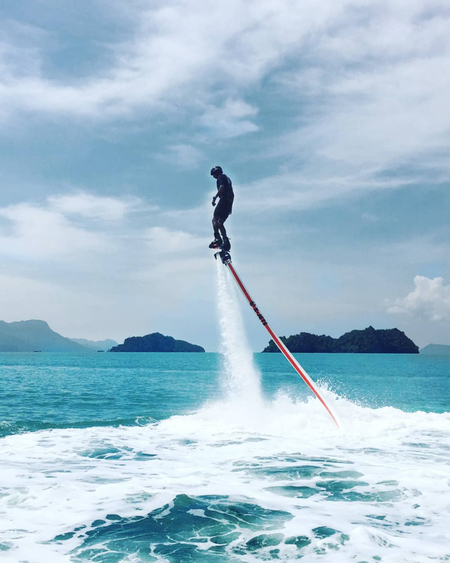 Water sprays as man soars above ocean attached to line, jet blade pack