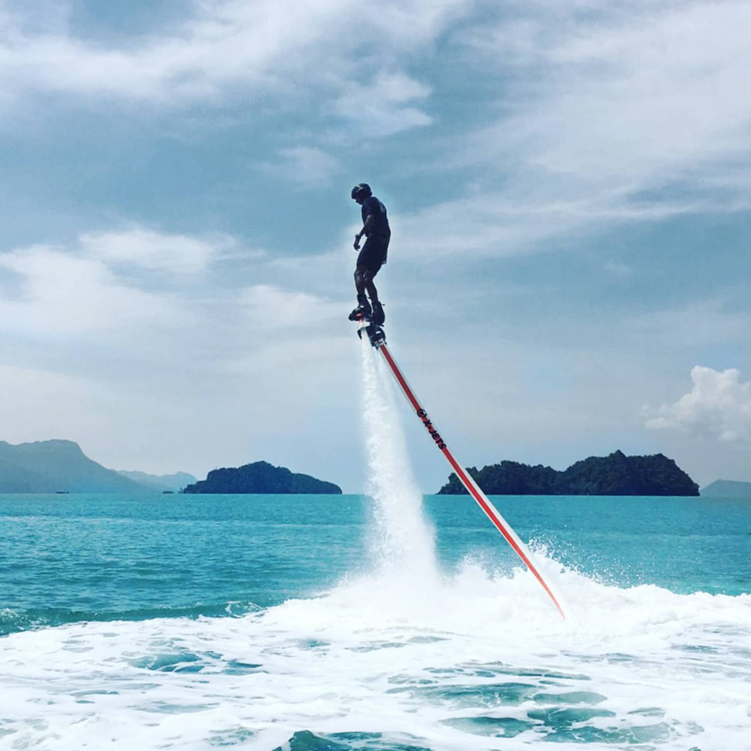 Water sprays as man soars above ocean attached to line, jet blade pack