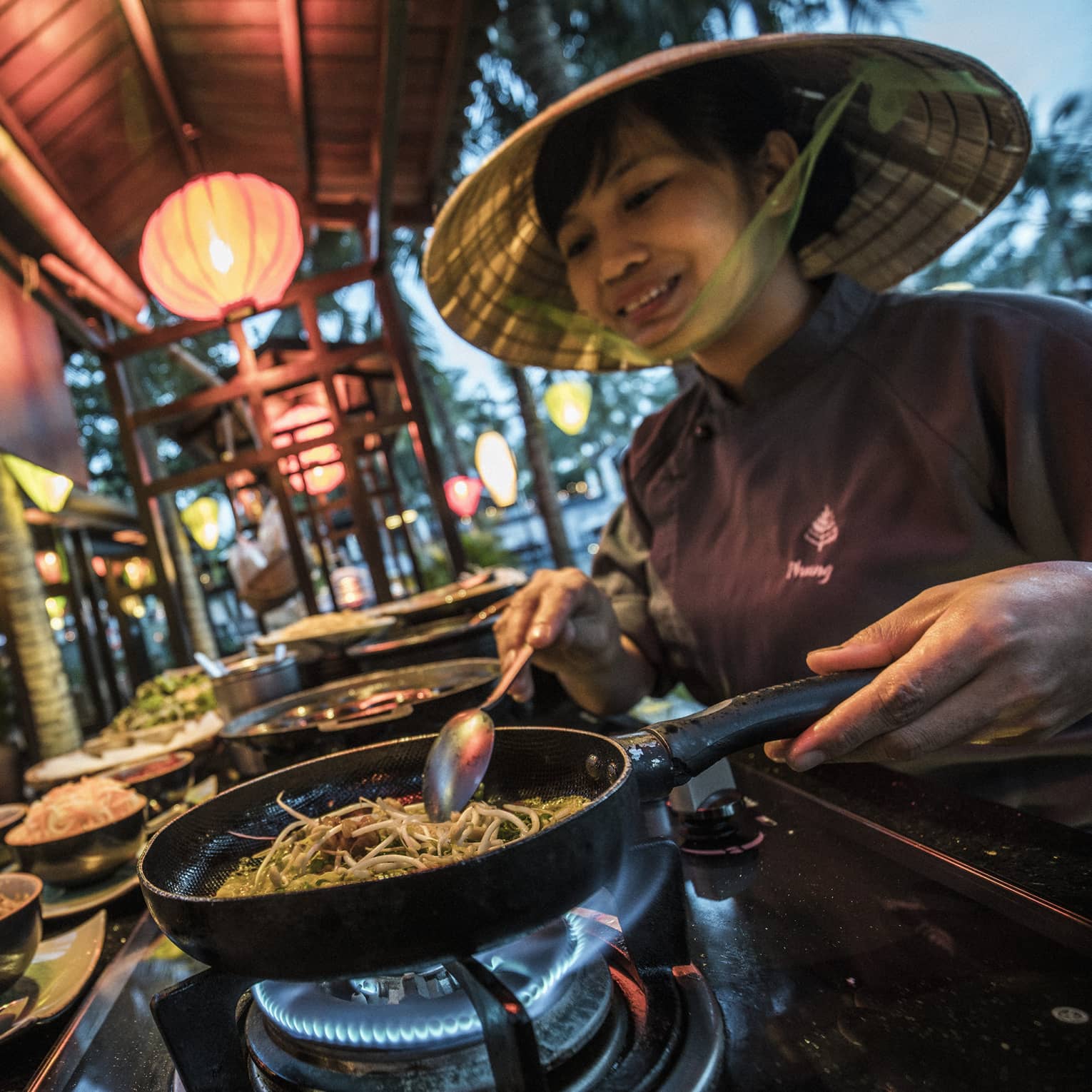 Chef cooks street food noodles in traditional Vietnamese rice hat