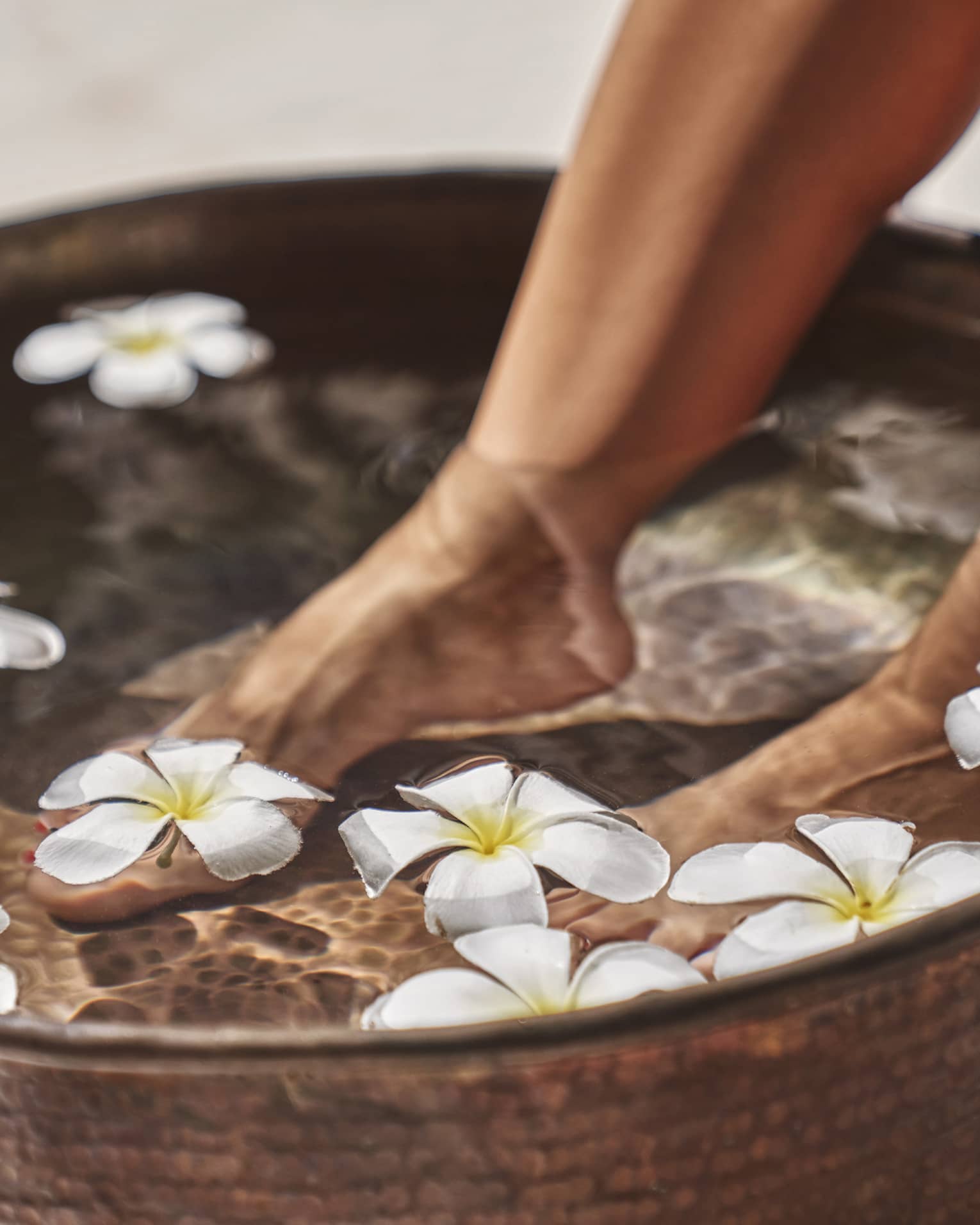 A woman's feet in a bowl of water and flowers.