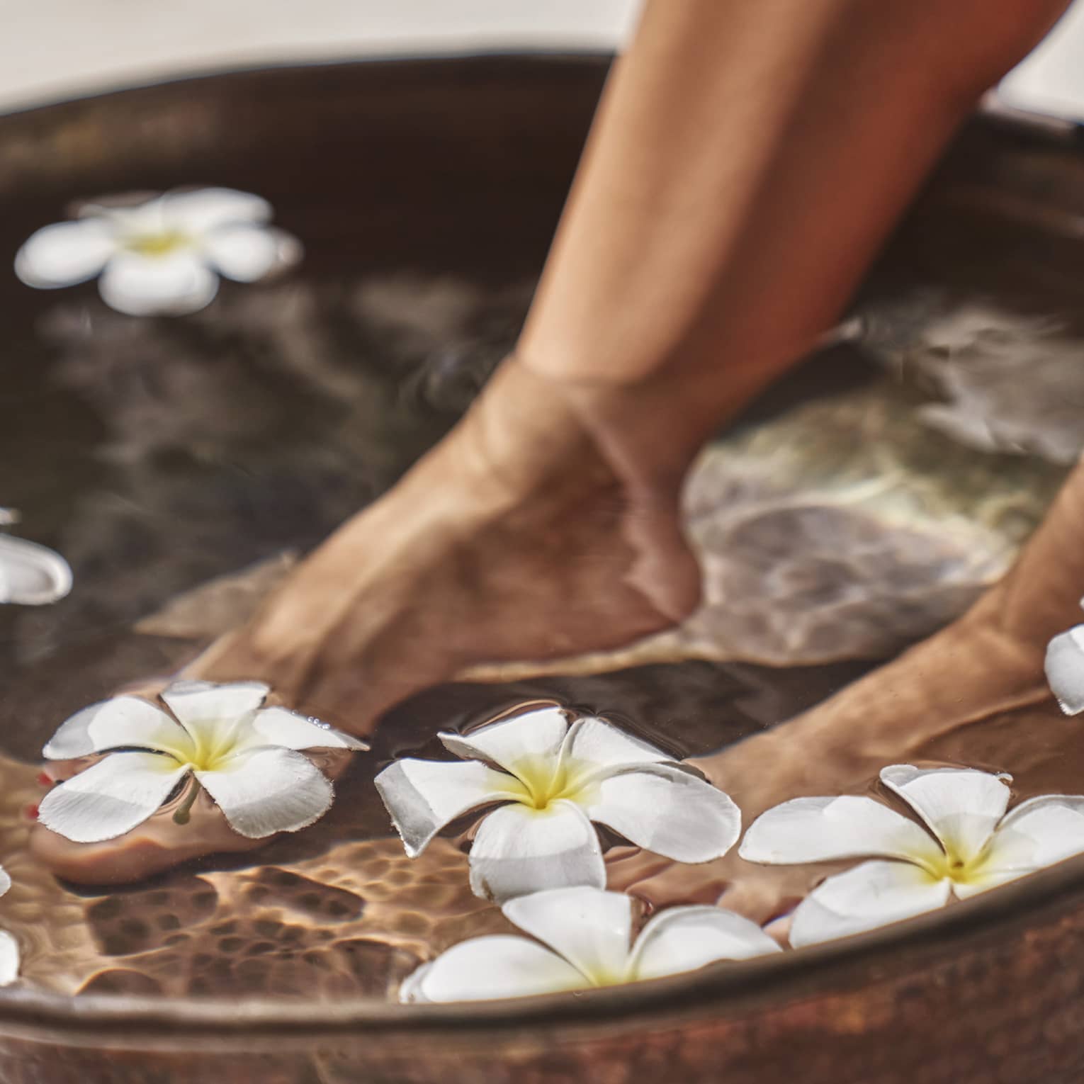 A woman's feet in a bowl of water and flowers.