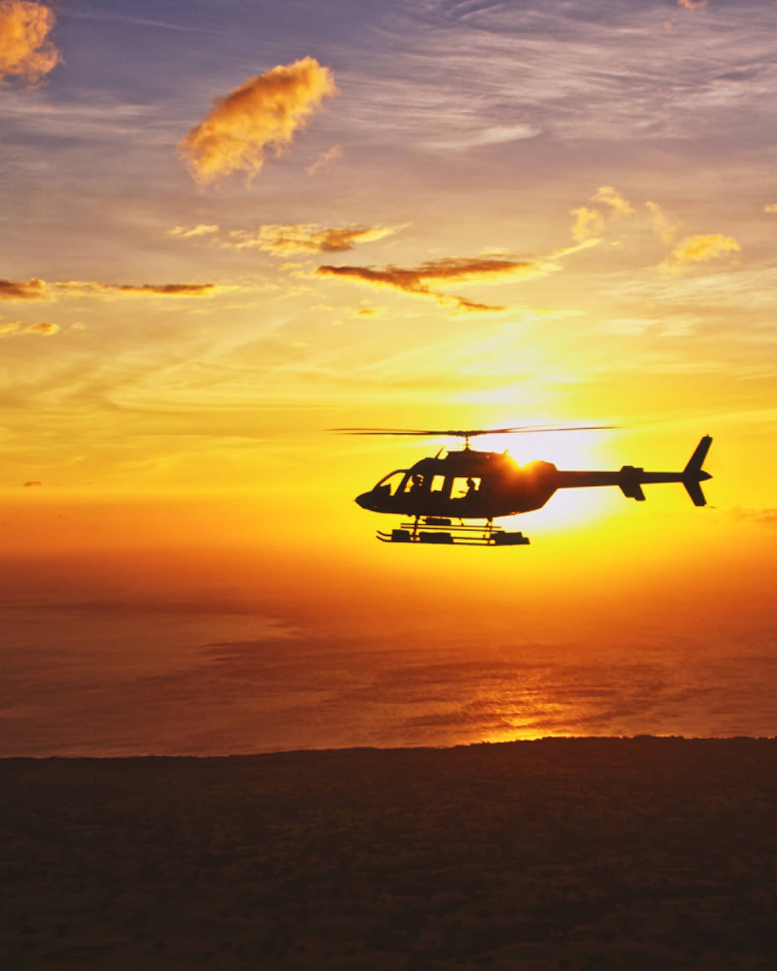 Silhouette of helicopter against orange sunset