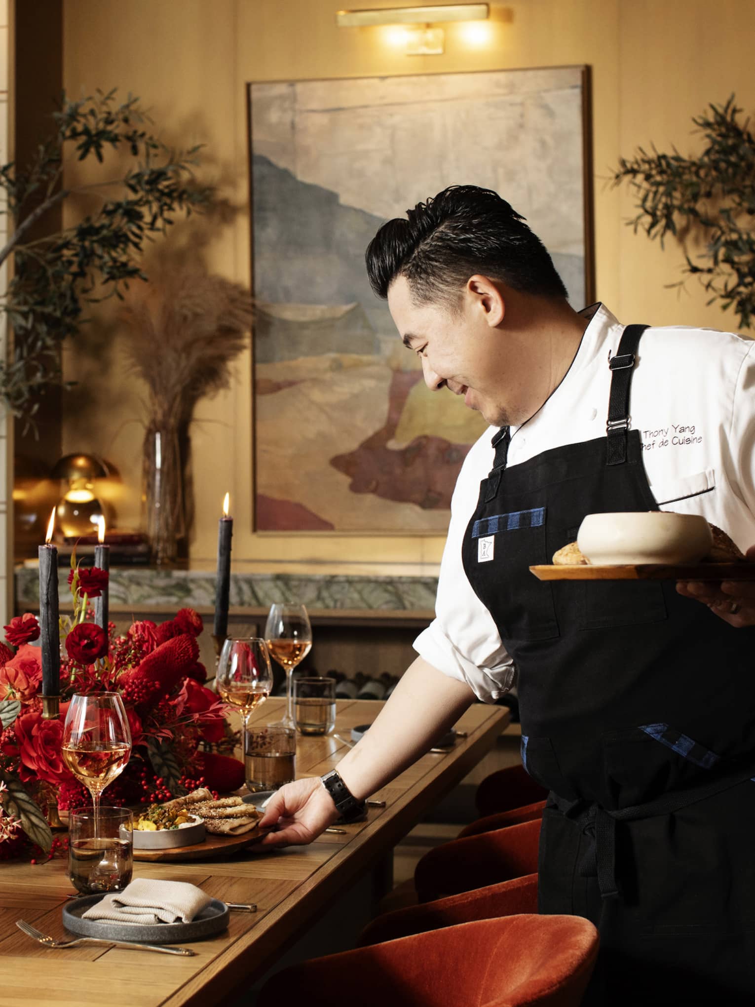 Chef putting dishes on a table with red flowers on it.