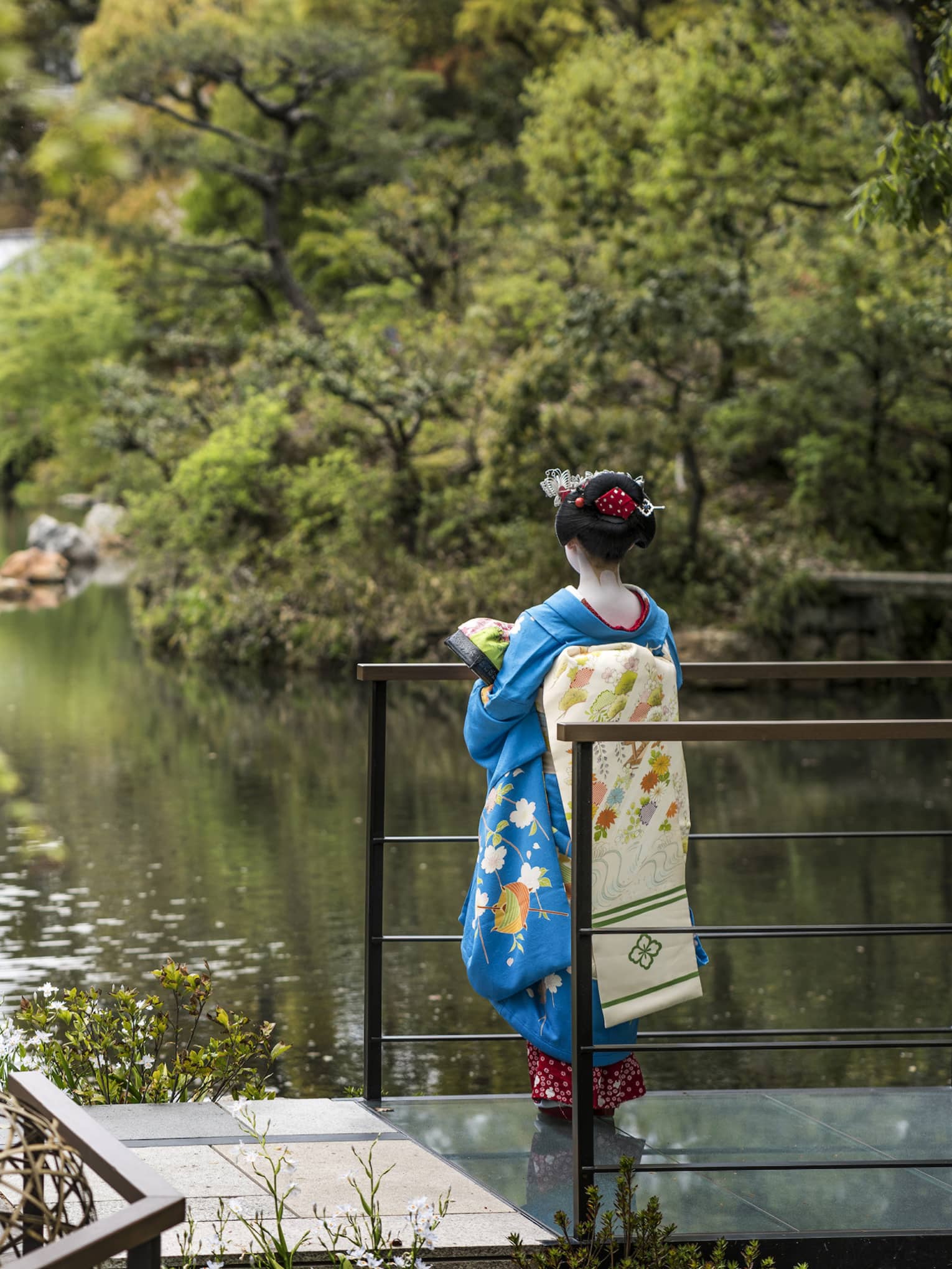 A woman in blue kimono gazing over the garden at Four Seasons Hotel Kyoto, a renowned luxury hotel in Kyoto.