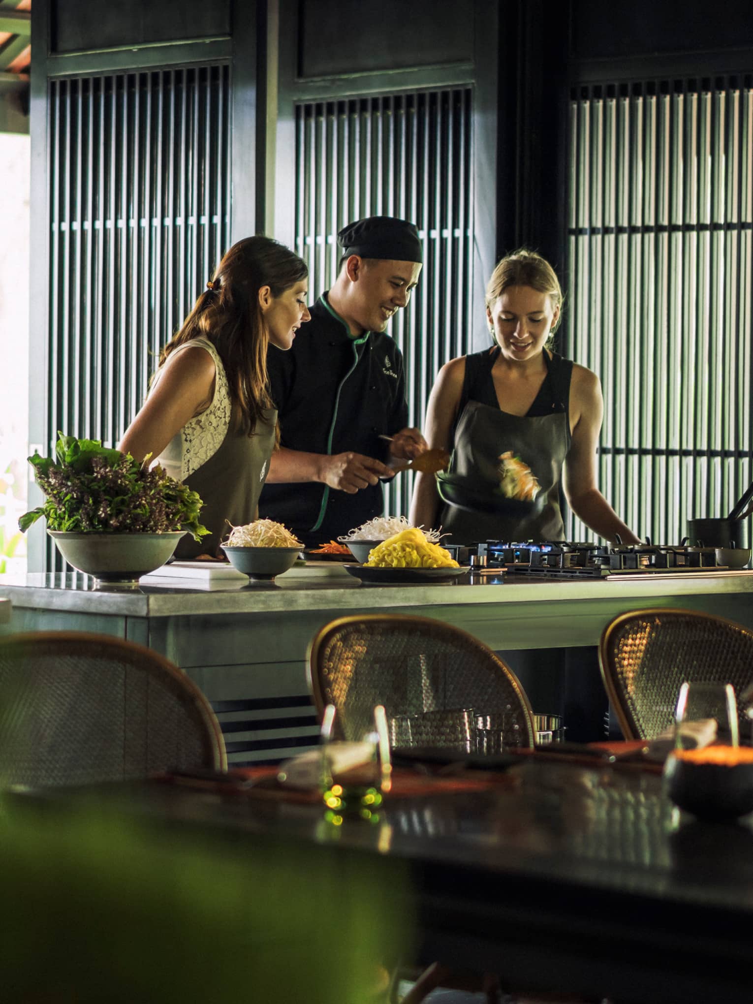 Chef, two women look at pan on kitchen range at Hoi An Cooking Academy 