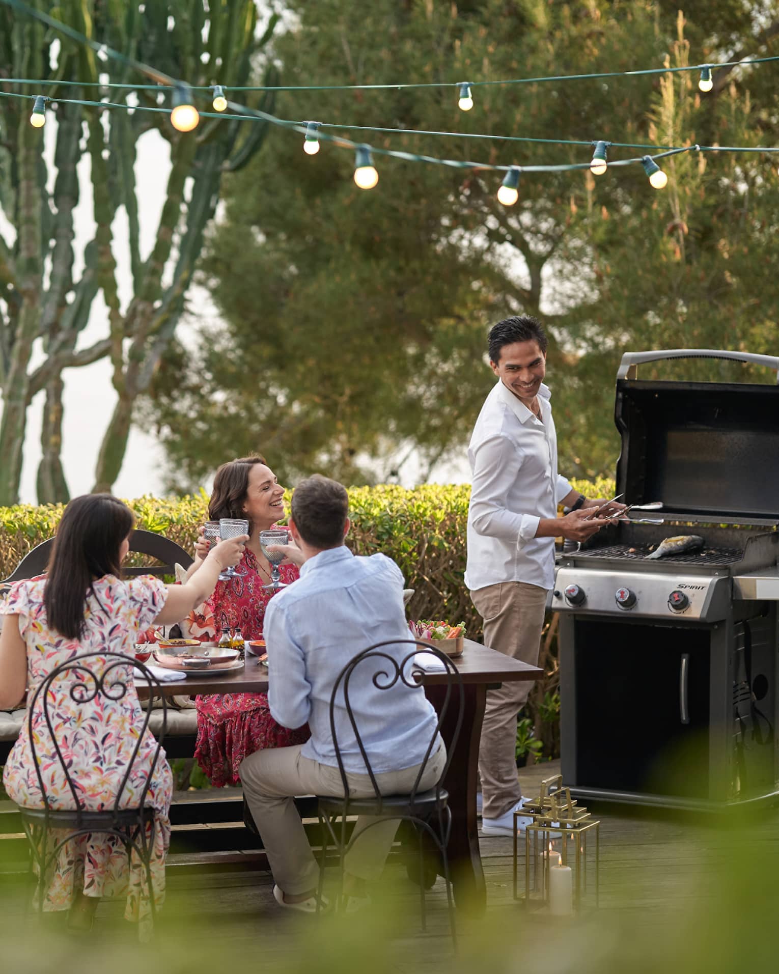 A group of four people grilling food outside at a large table while wearing nice beach clothes.