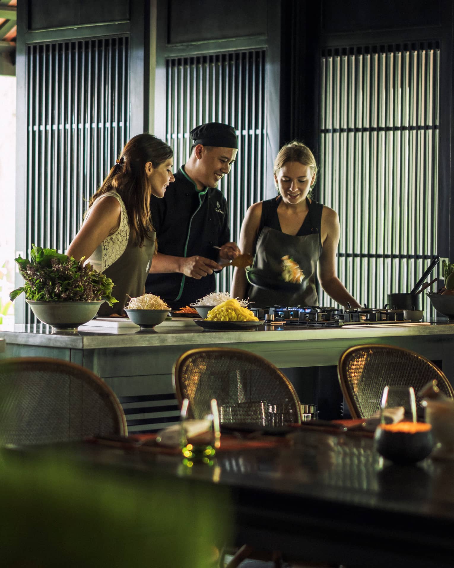 Chef, two women look at pan on kitchen range at Hoi An Cooking Academy 