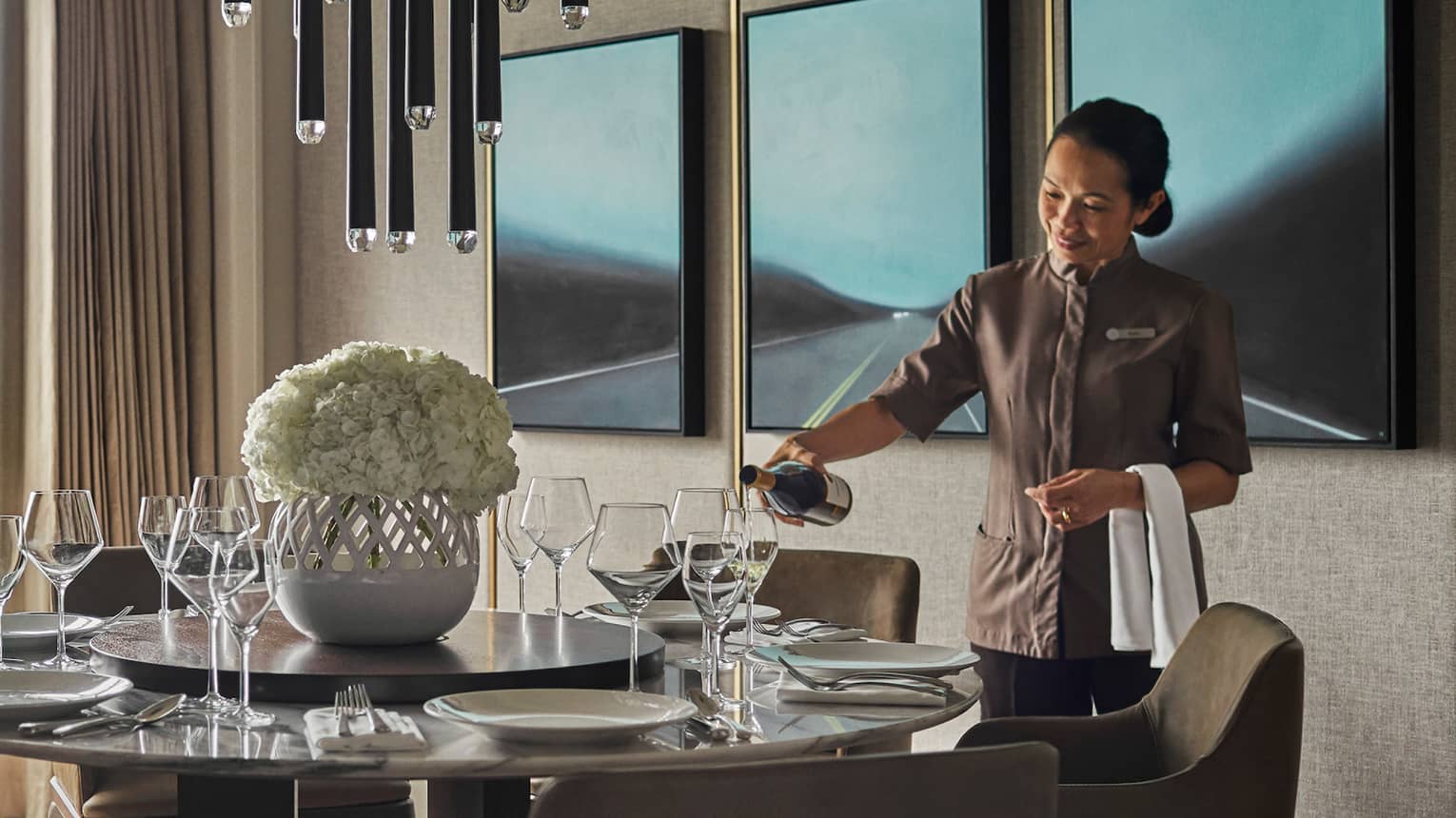 Hotel staff pours wine in glass at round dining table by floor-to-ceiling window