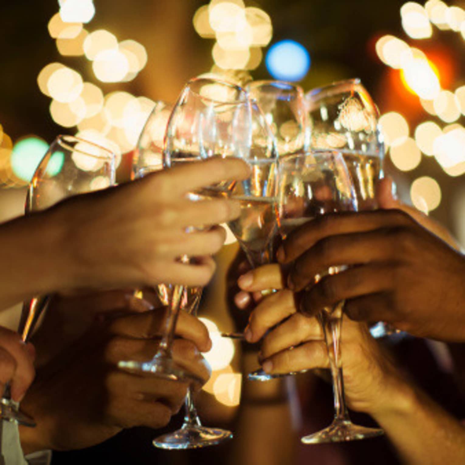 A group of guests clink their glasses of champagne together on a patio with twinkle lights