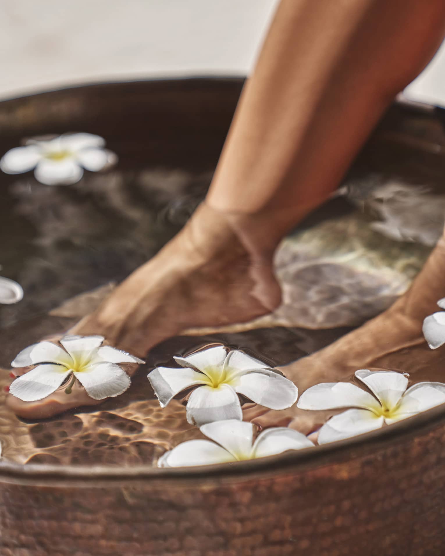 A woman's feet in a bowl of water and flowers.