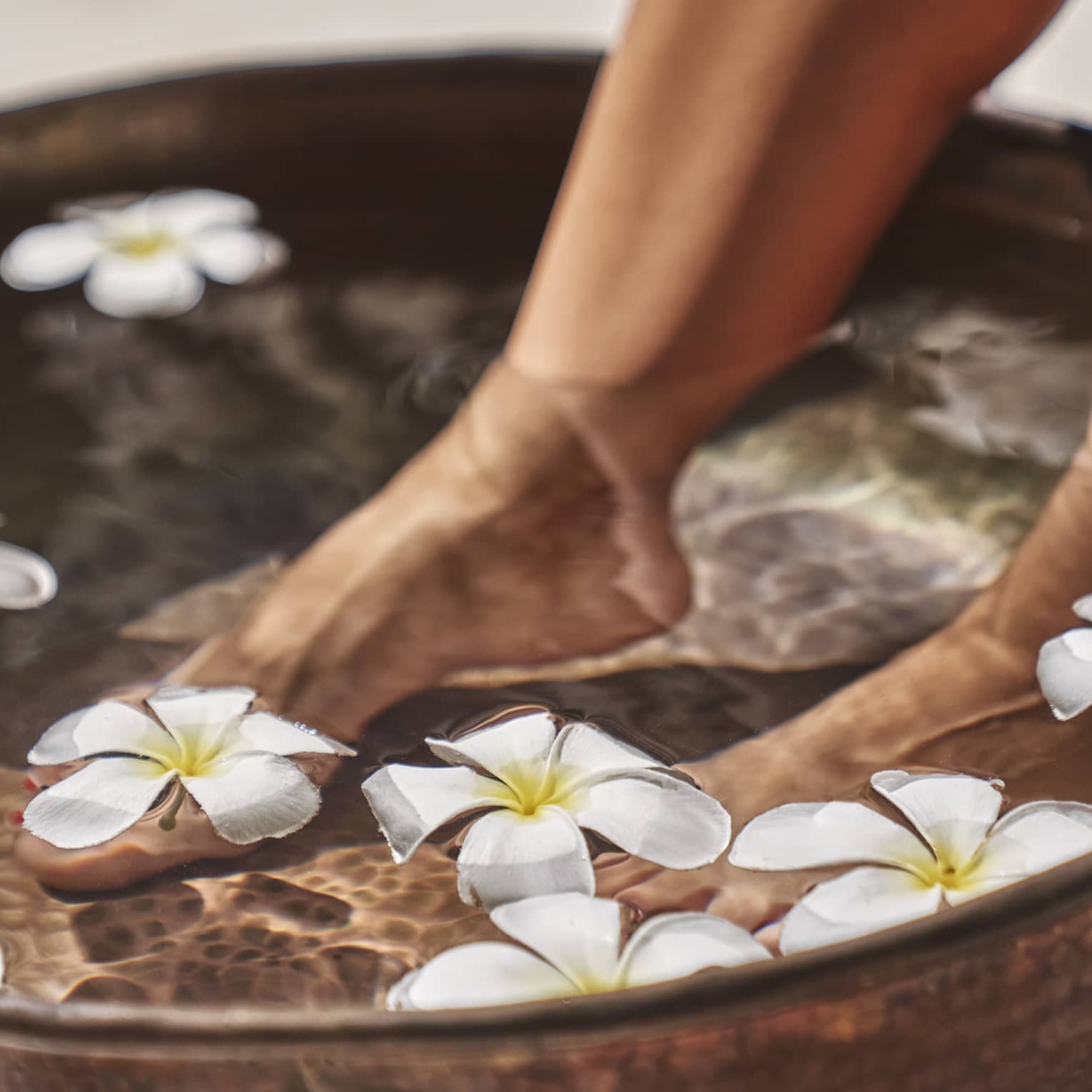 A woman's feet in a bowl of water and flowers.
