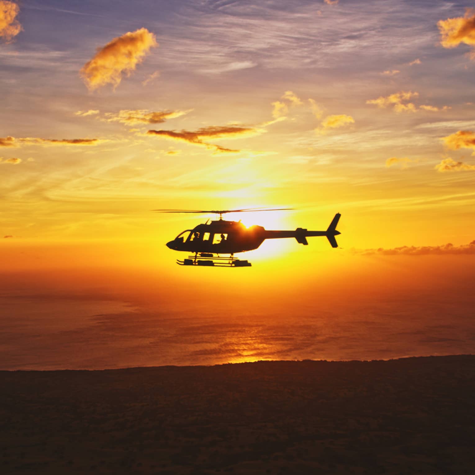 Silhouette of helicopter against orange sunset