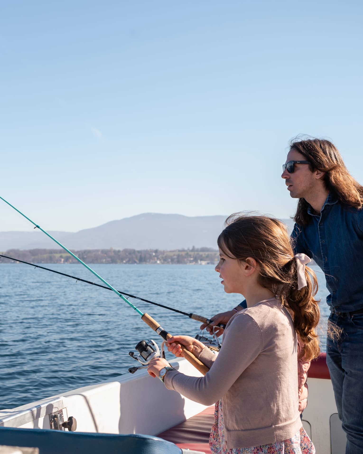 Man holding net and fishing rod, and girl standing in boat, holding fishing rod