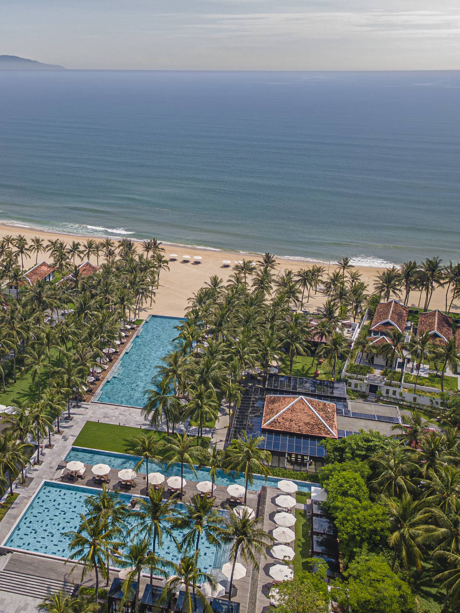 Aerial view of beachside property with pools, palm trees and ocean views