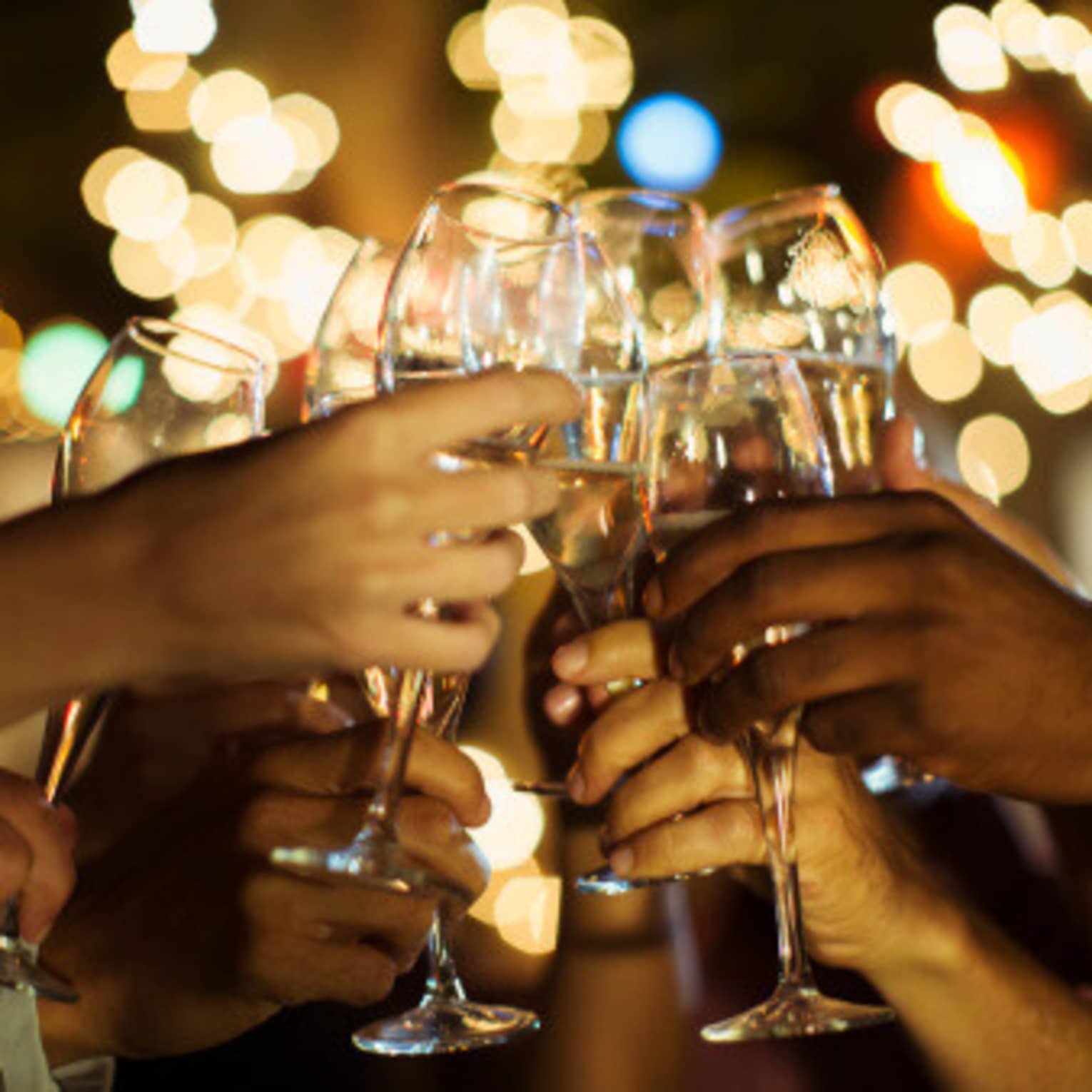 A group of guests clink their glasses of champagne together on a patio with twinkle lights
