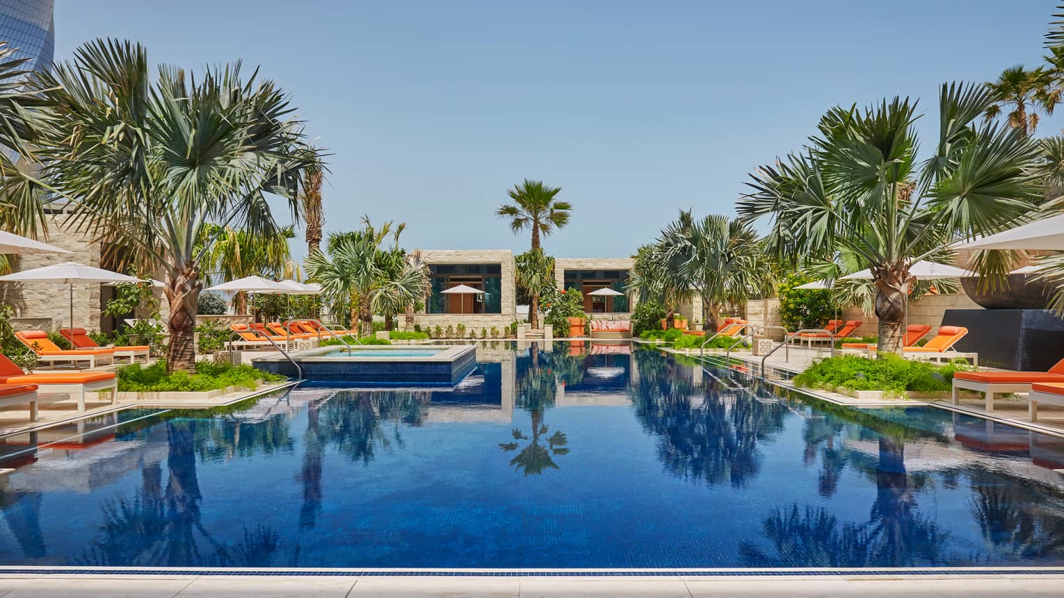 Azure adults-only swimming pool, surrounded by palm trees, orange lounge chairs, cabanas