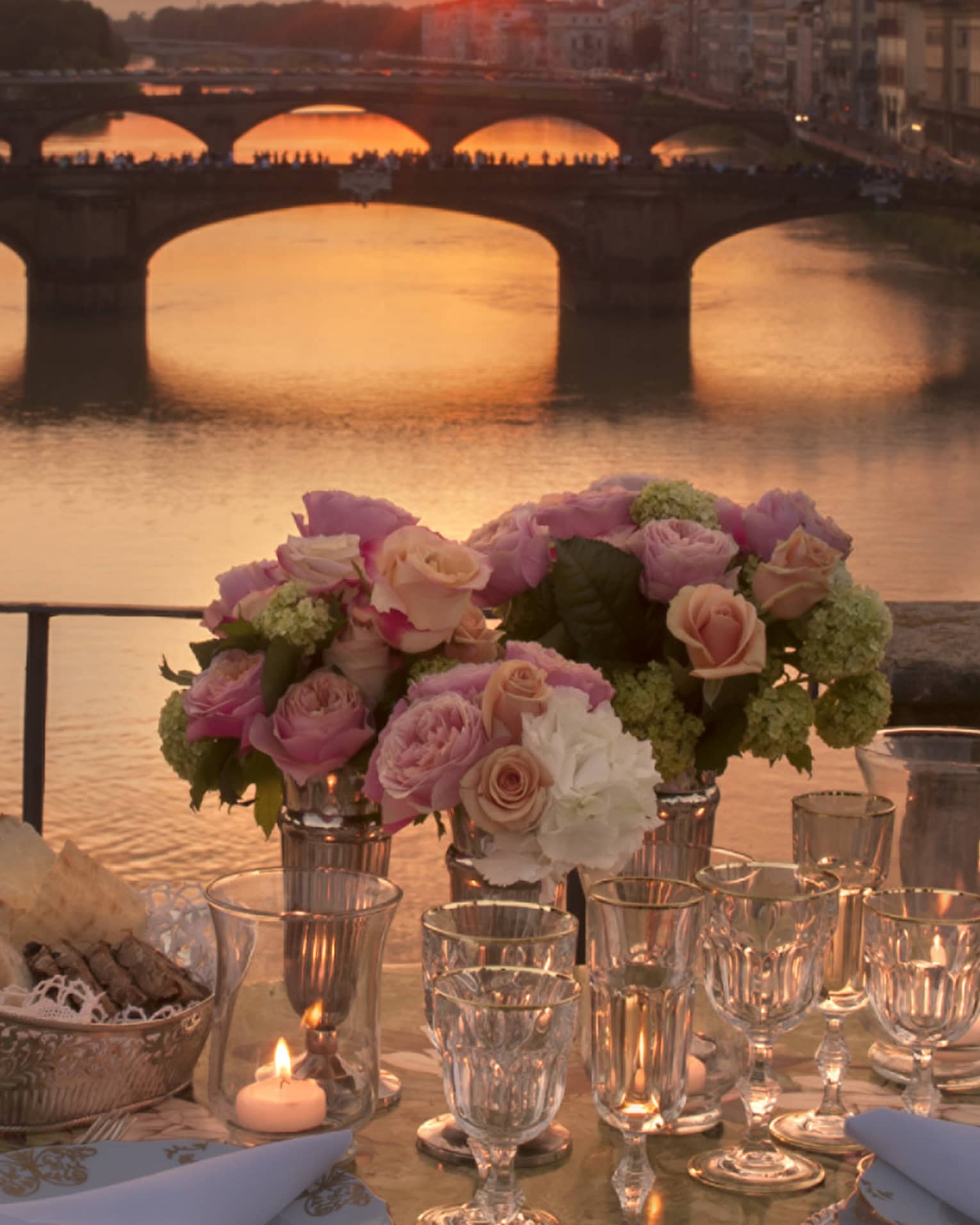 Pink roses in vases on formal dining table on bridge overlooking canal, sunset