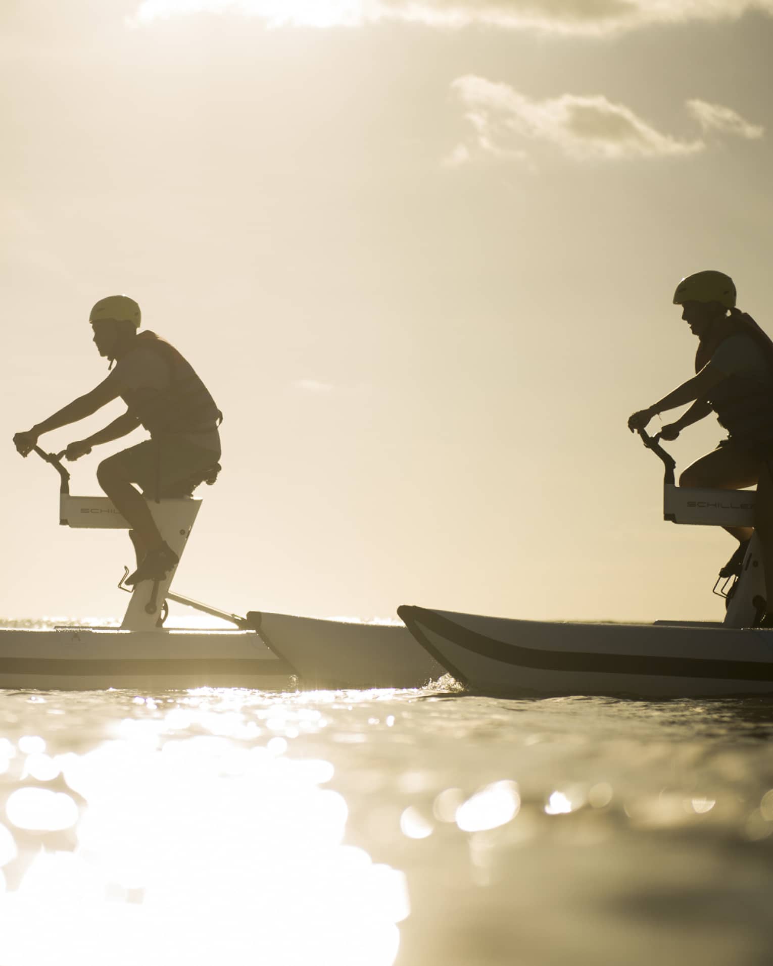 Silhouettes of two men riding aquatic bicycles on ocean at sunset