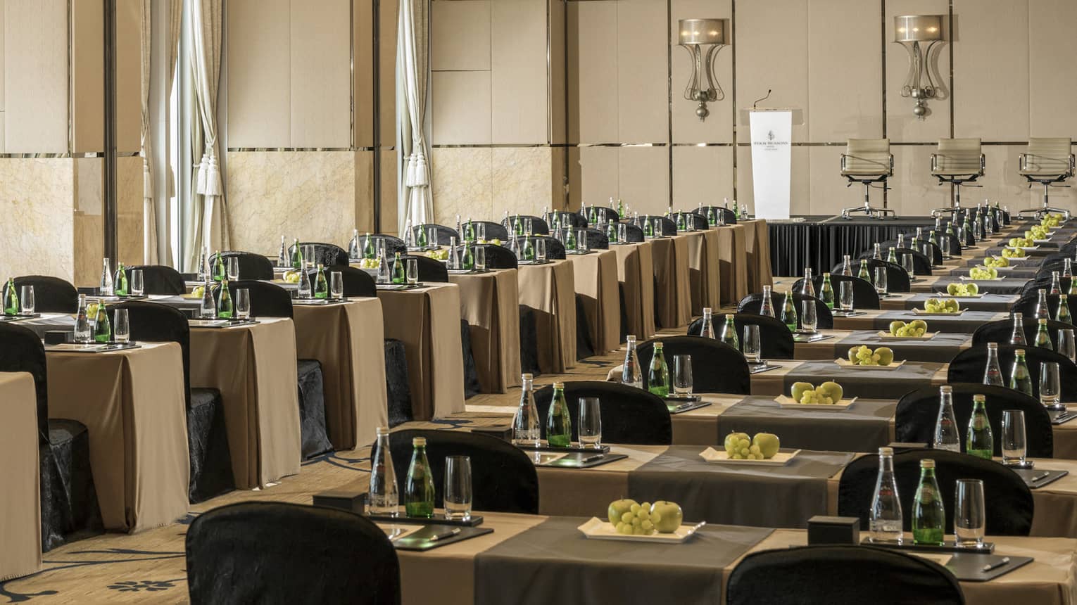 Rows of conference tables and chairs under high ceilings, tall windows in large ballroom