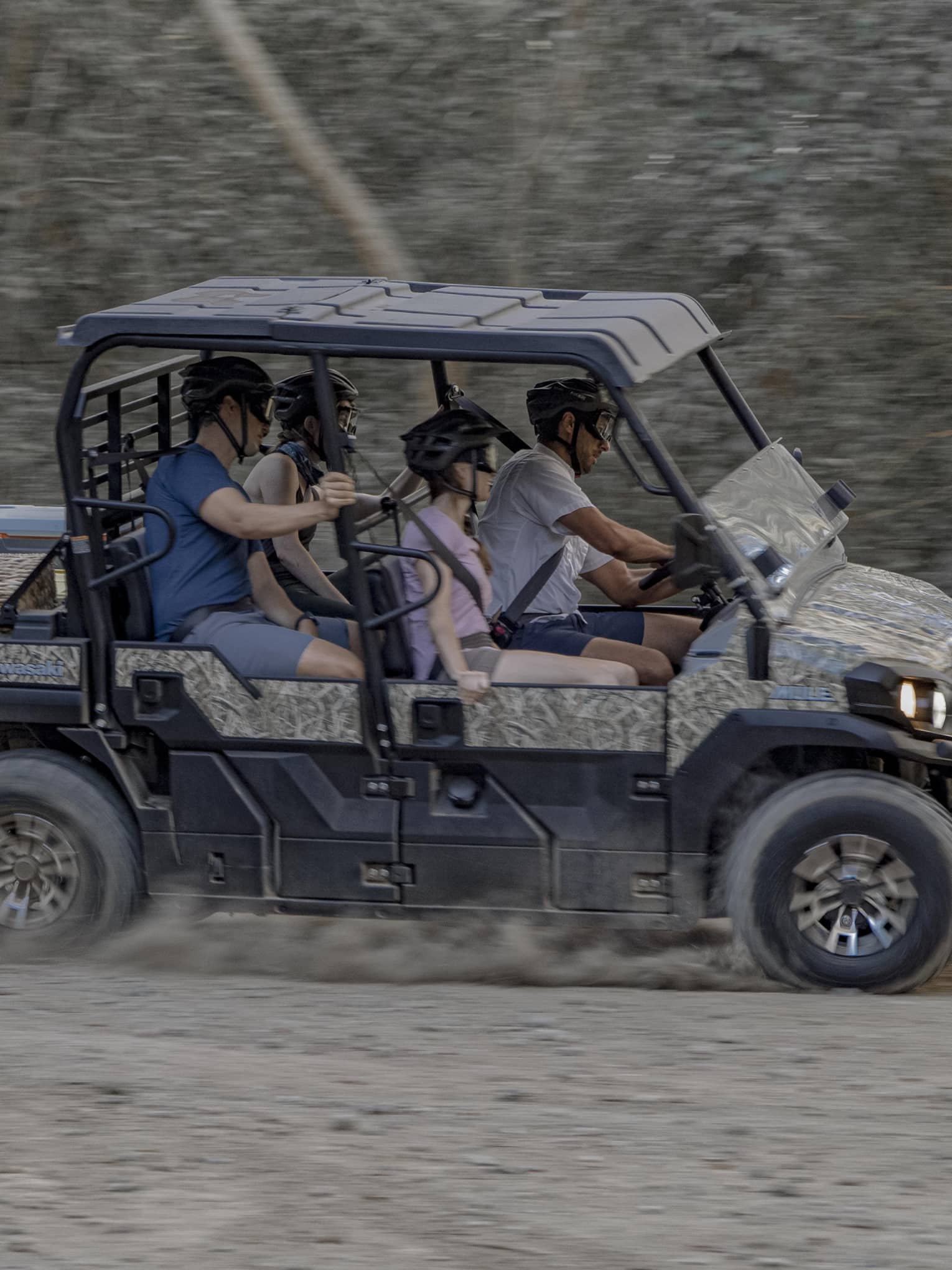 Four people speed along a dirt road in a 4x4 vehicle