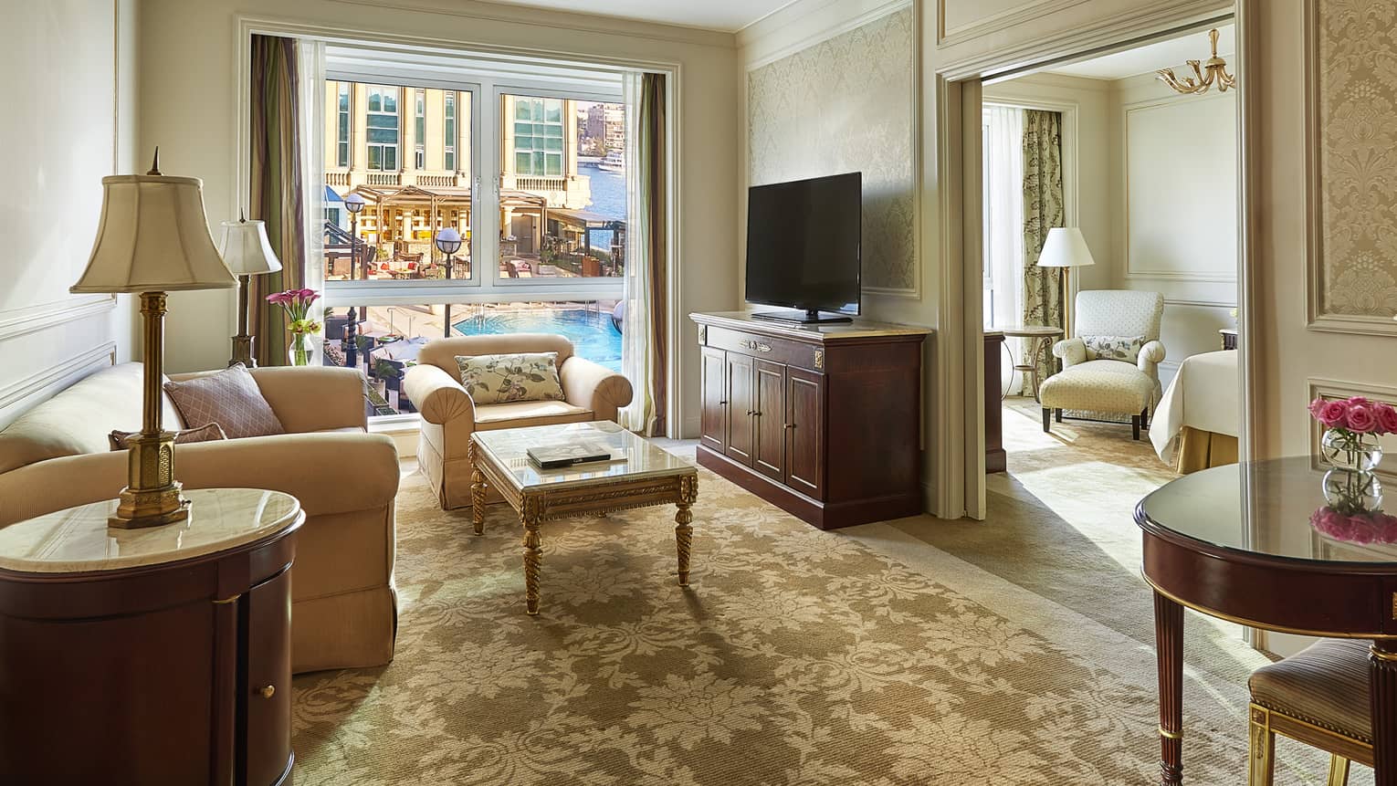 Four Seasons Executive Suite living room with plush sofa, armchairs, window overlooking patio, pool