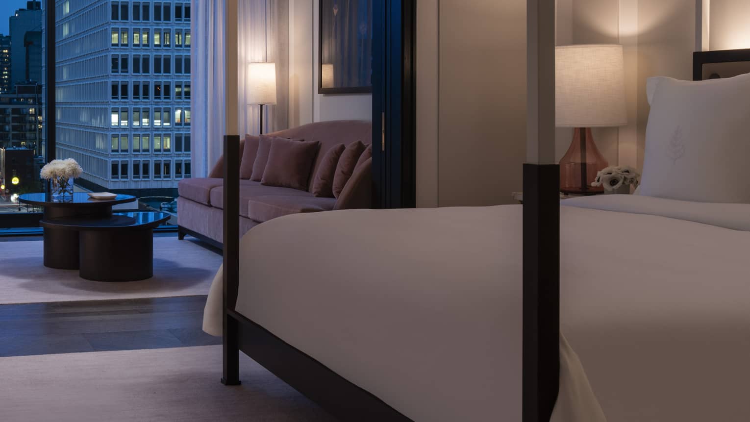 Presidential Suite dimly lit and with all-white modern four-poster bed and evening balcony view