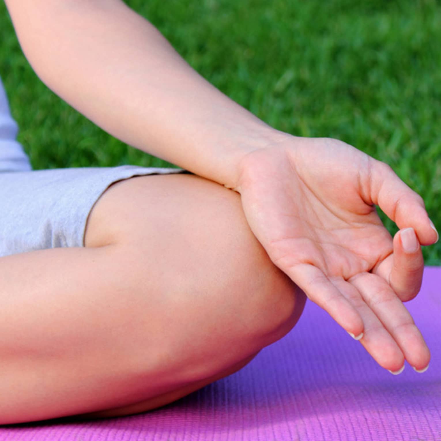Side of hand, leg in cross legged meditation pose on yoga mat 