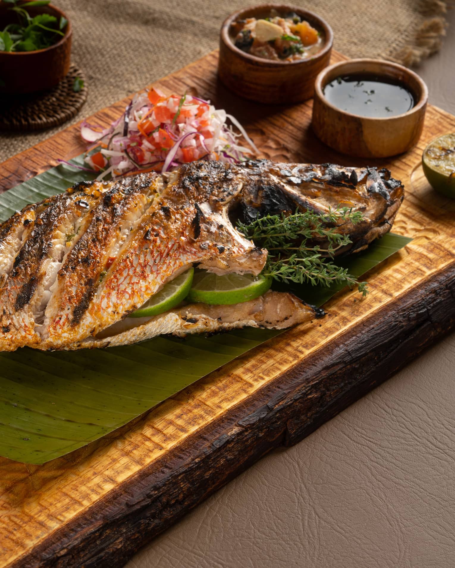 Whole Grilled Snapper served on a wooden plank along with an assortment of condiments and sauces