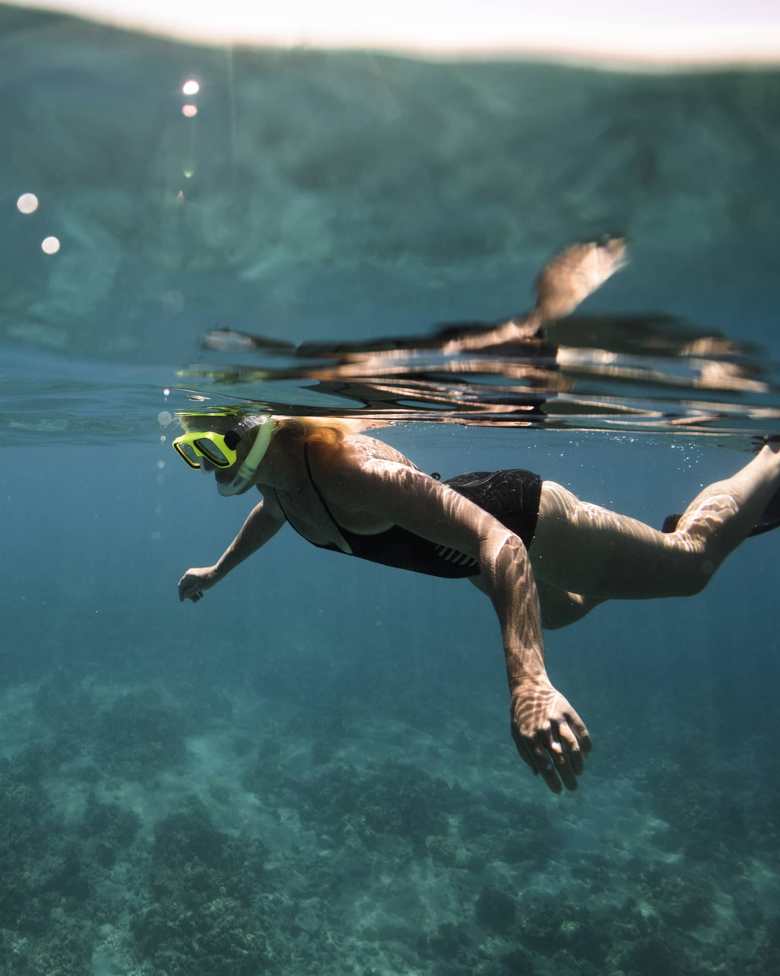 Underwater view of woman with snorkel, mask over coral reef