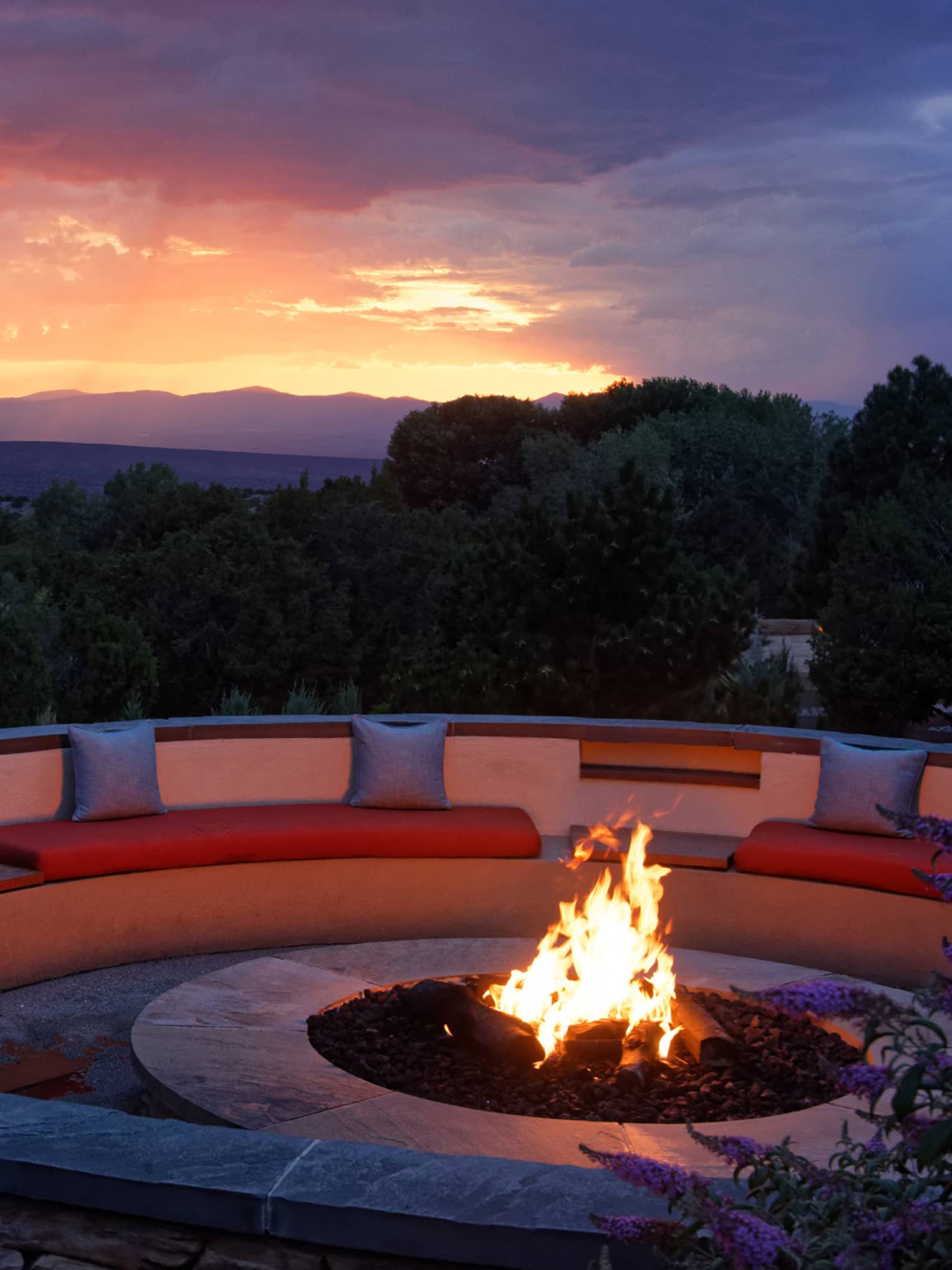Fire pit with seating surrounding it and a sunset in the background.