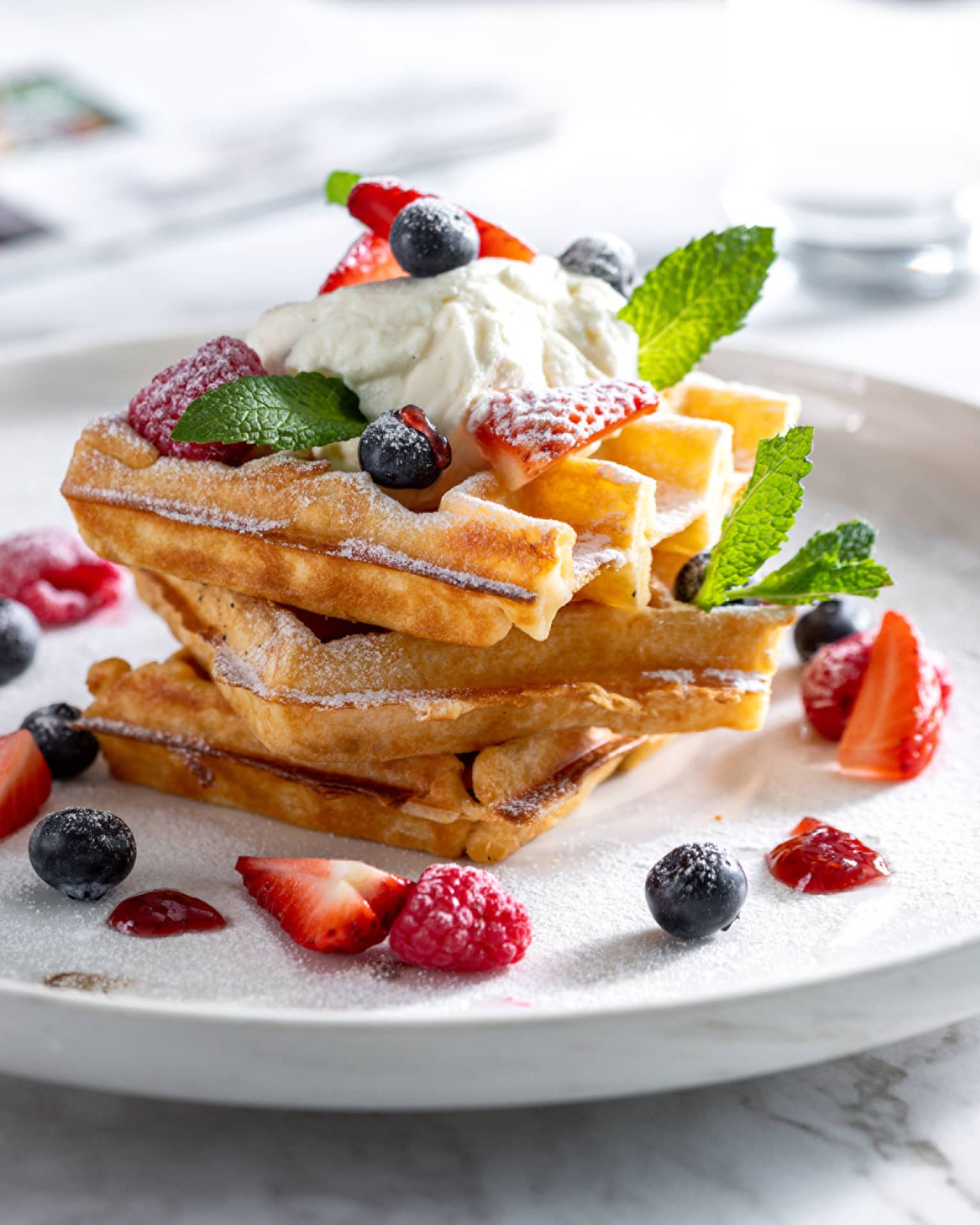 Stack of Belgian waffles with fresh berries and topped with cr�me fra�che and mint springs on round white plate