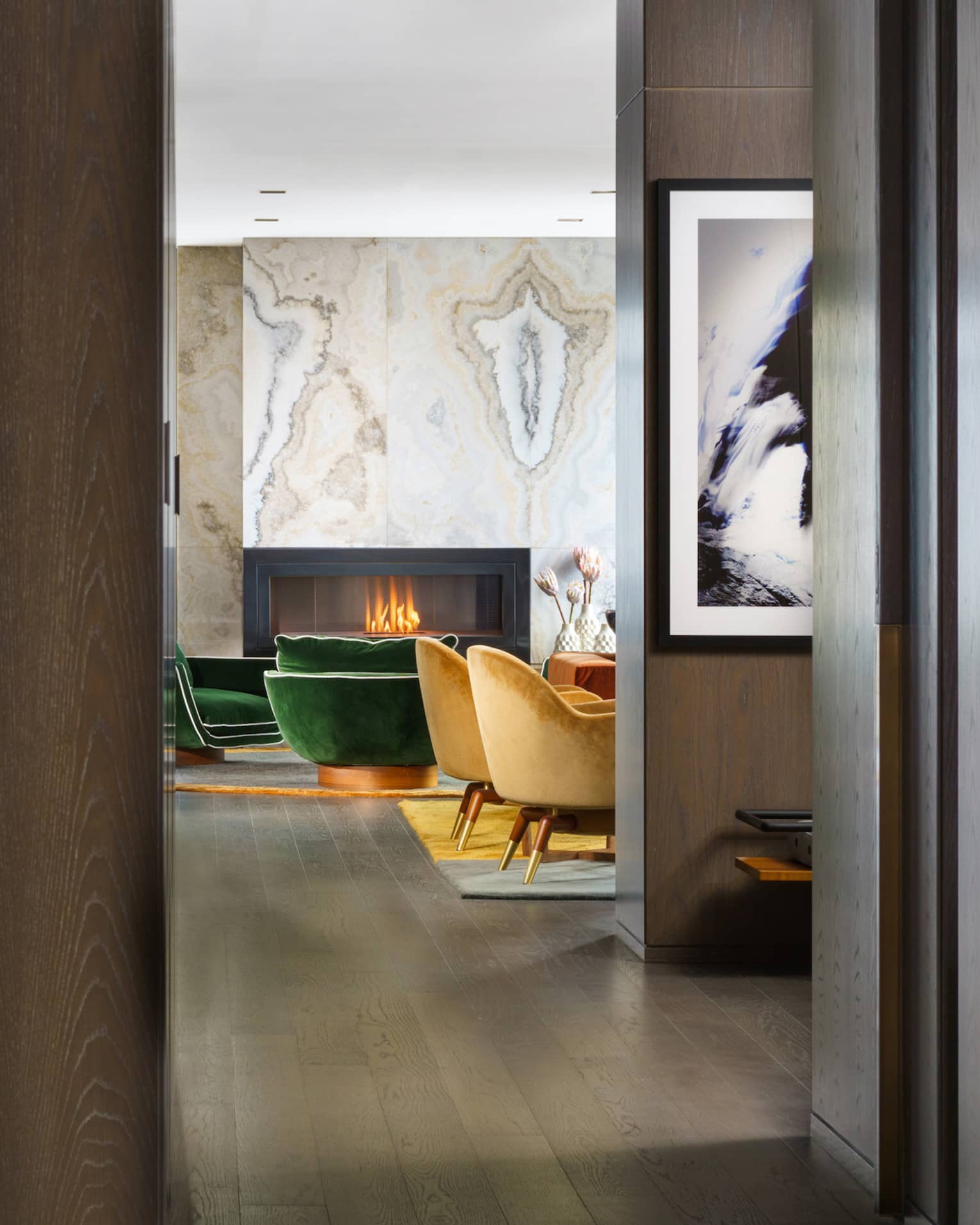 Entryway to suite, dark wood floors, mustard- and emerald green-coloured arm chairs by fireplace