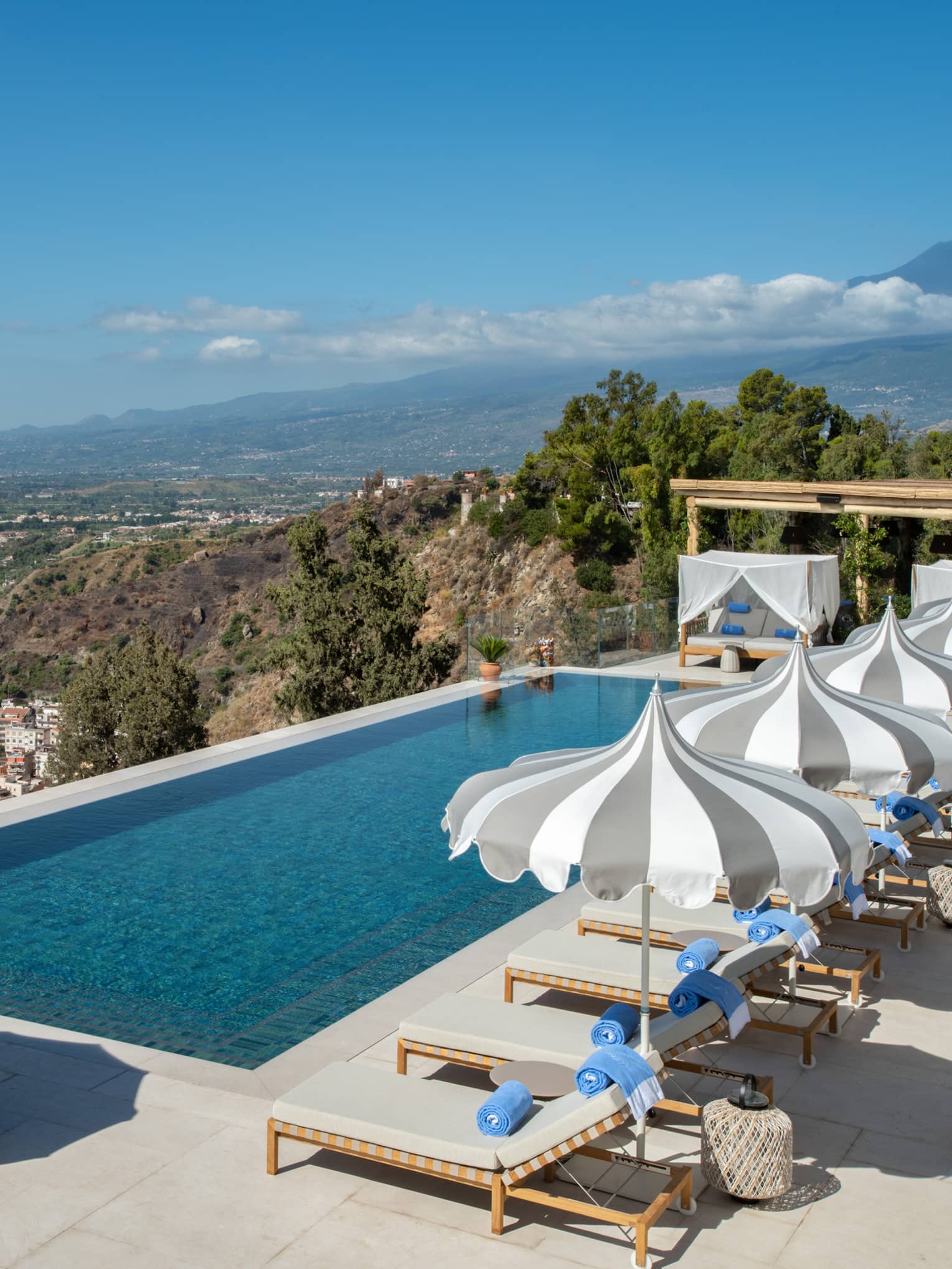 Rectangular pool, lounge chairs and umbrellas overlooking sea and Mount Etna