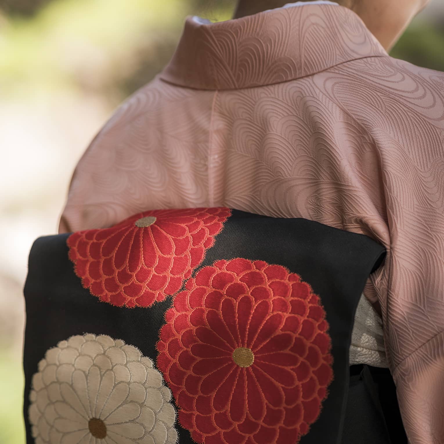 Back view of a person wearing a pink kimono with a black obi featuring red and white floral designs