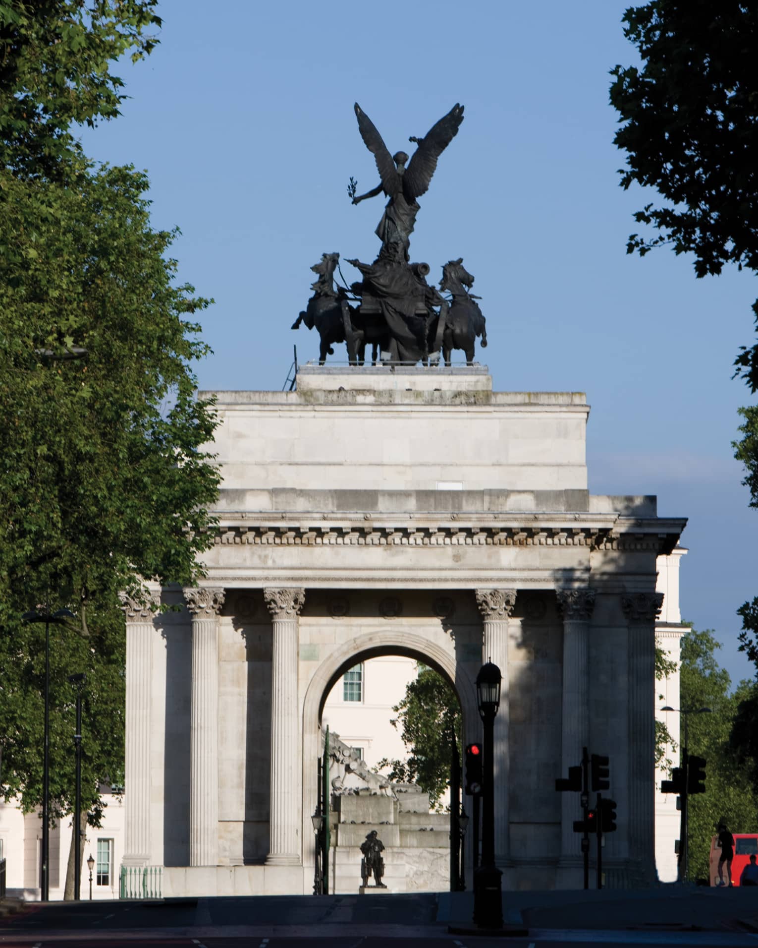 View through trees to Wellington Arch monument and statue against blue sky