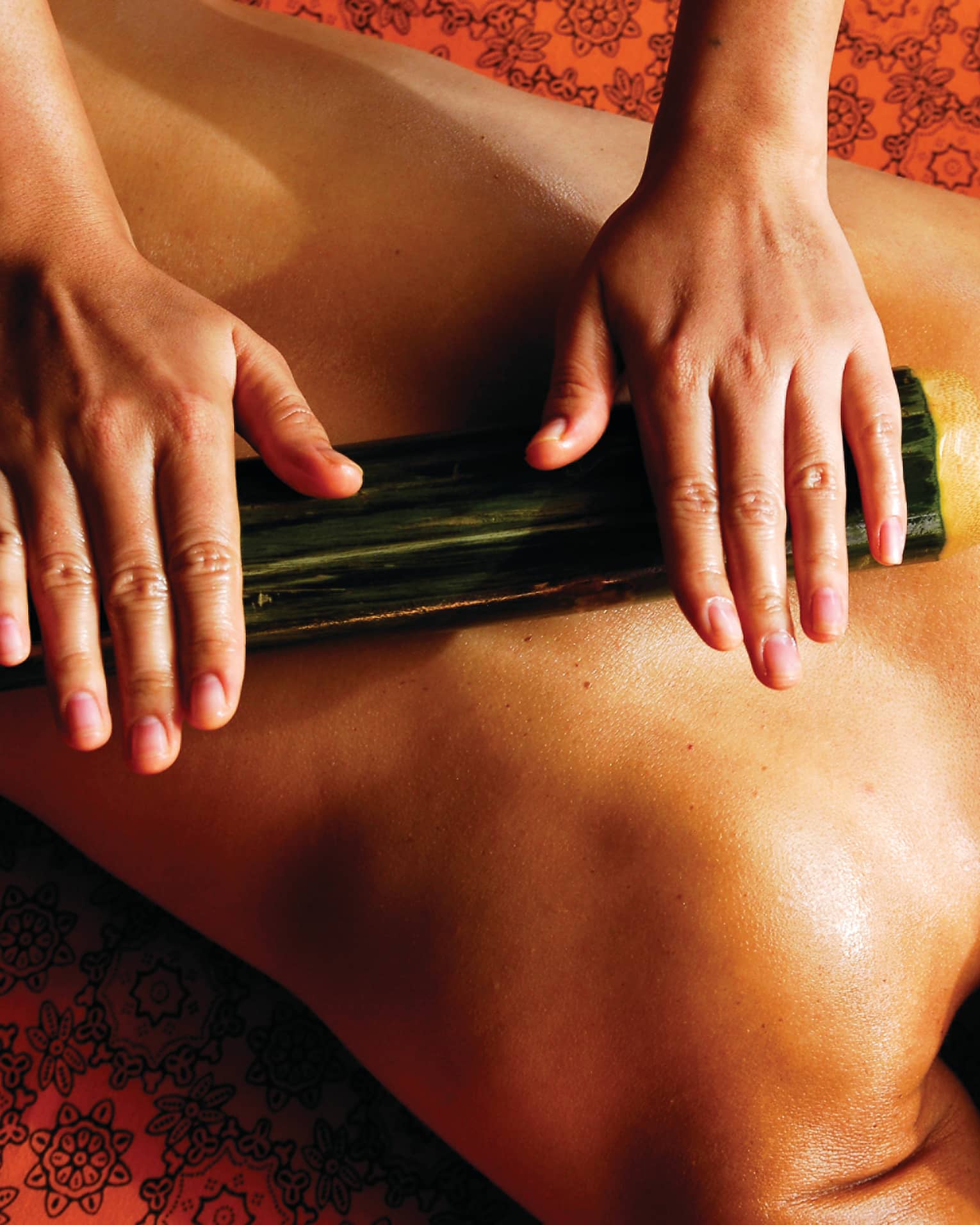 Spa staff rolls thick bamboo stick over woman's bare back, shoulders