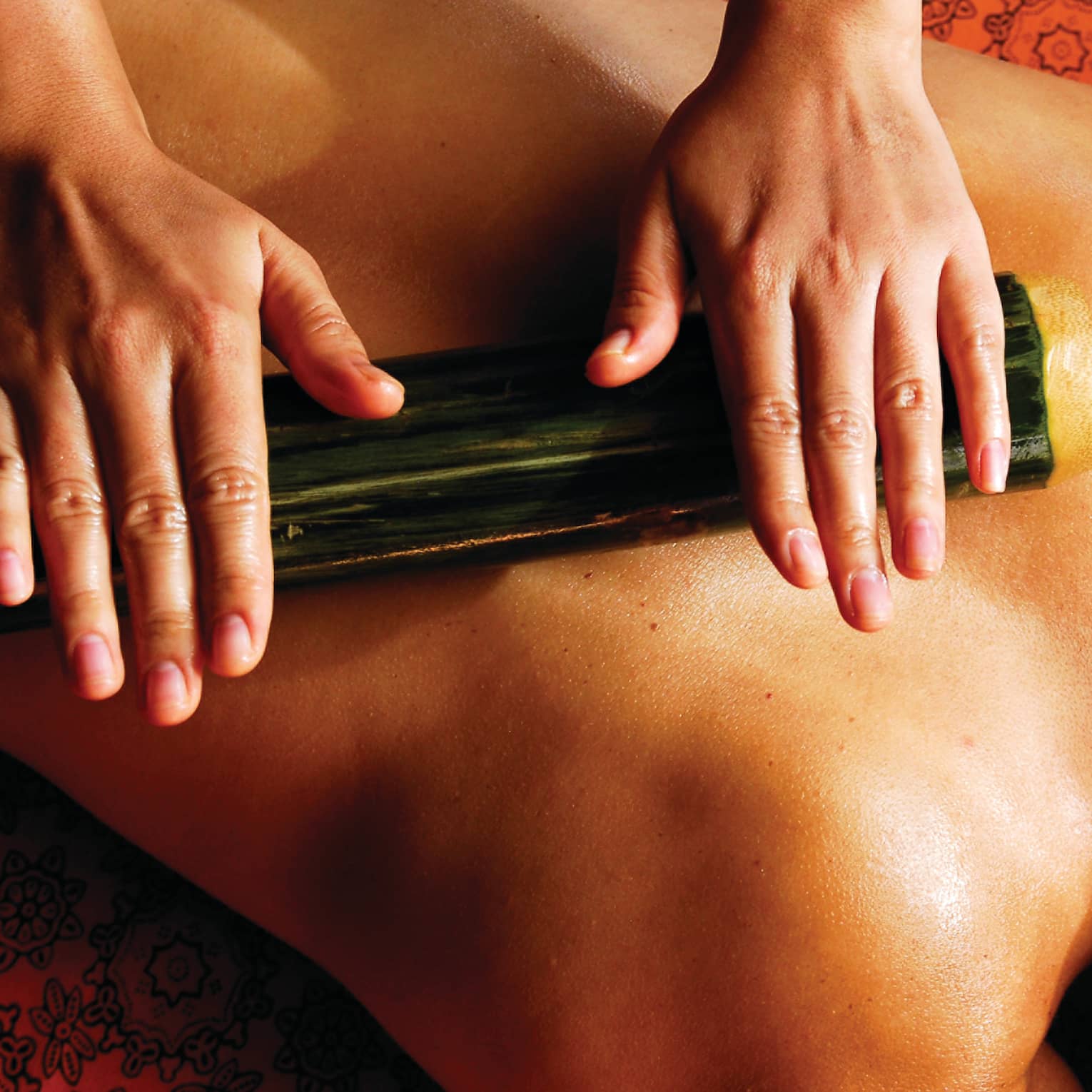 Spa staff rolls thick bamboo stick over woman's bare back, shoulders
