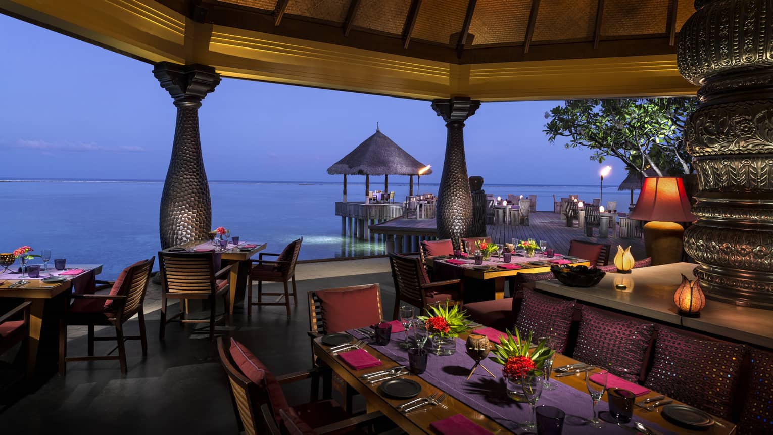 Evening view of Baraabaru restaurant dining patio on the water, with tropical flower arrangements, lanterns