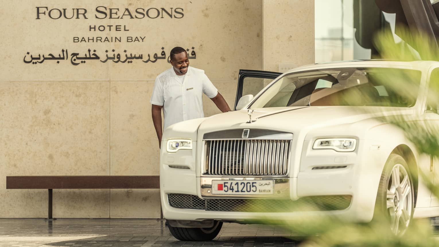 Front entrance, hotel staff opens door of luxury white car by Four Seasons Hotel Bahrain Bay sign