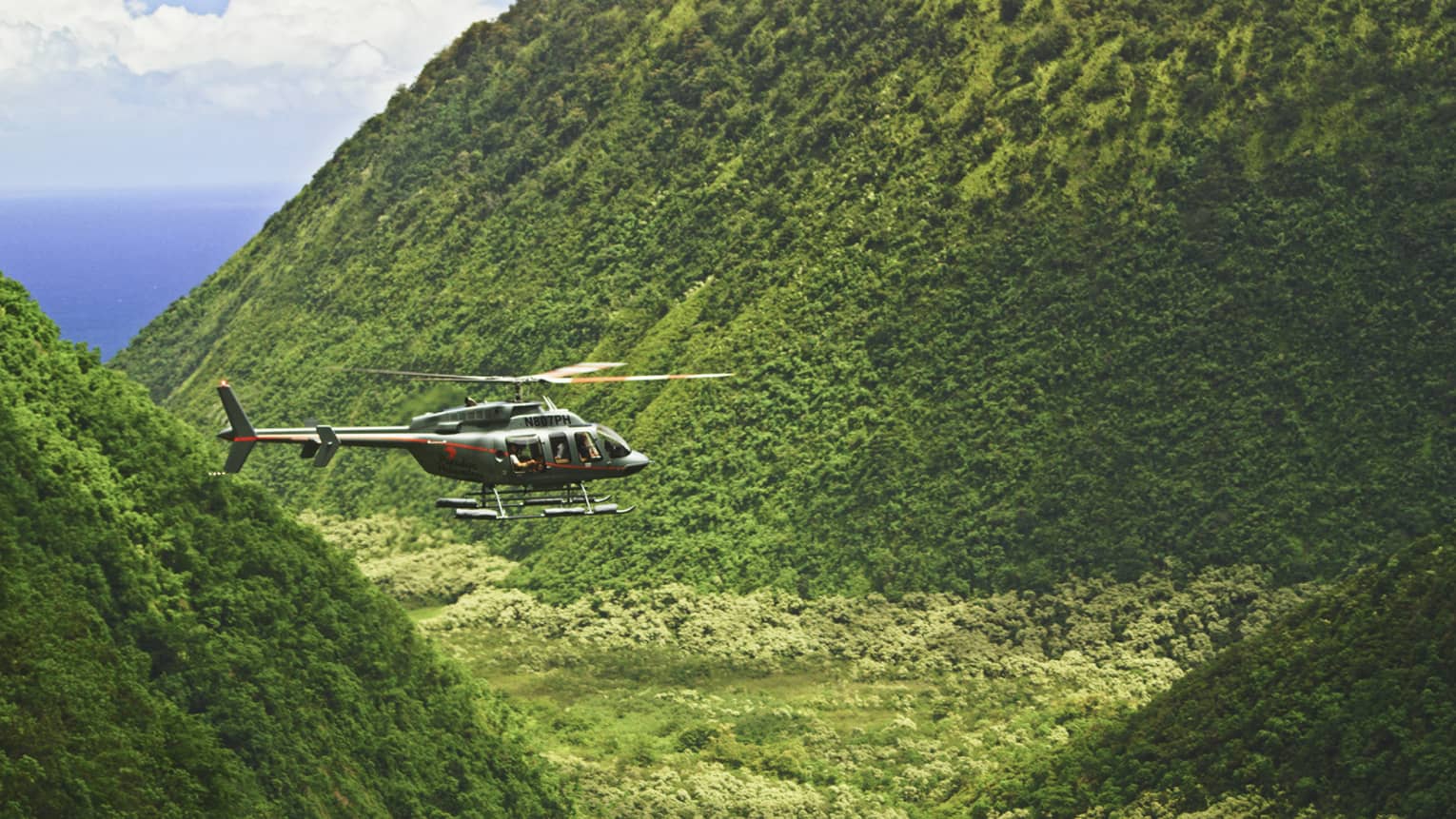 Orange and grey helicopter flying through crevice between green mountains