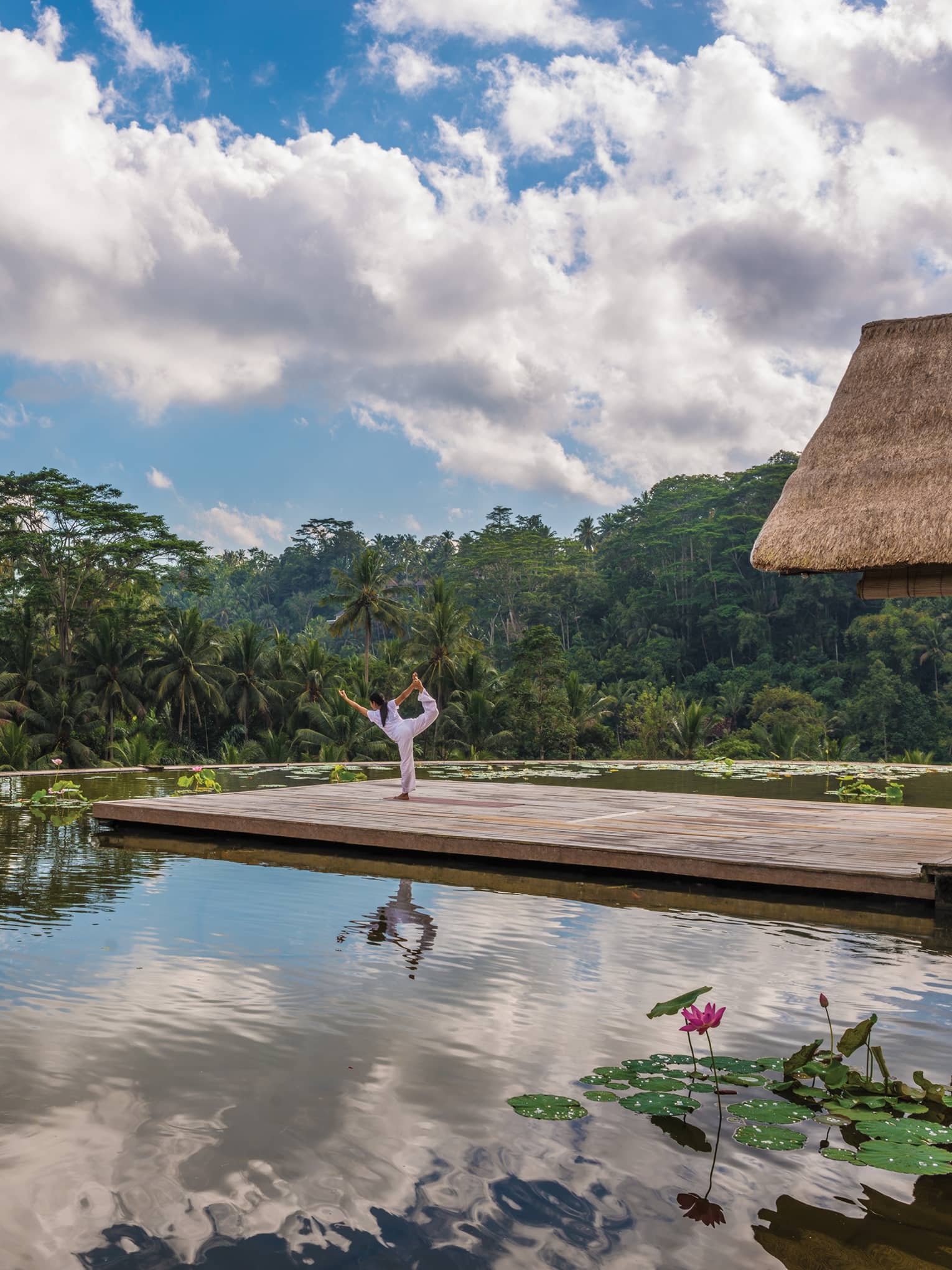 A guest does yoga on the roof of Four Seasons Resort Bali Sayan with a blue sky reflected in the water