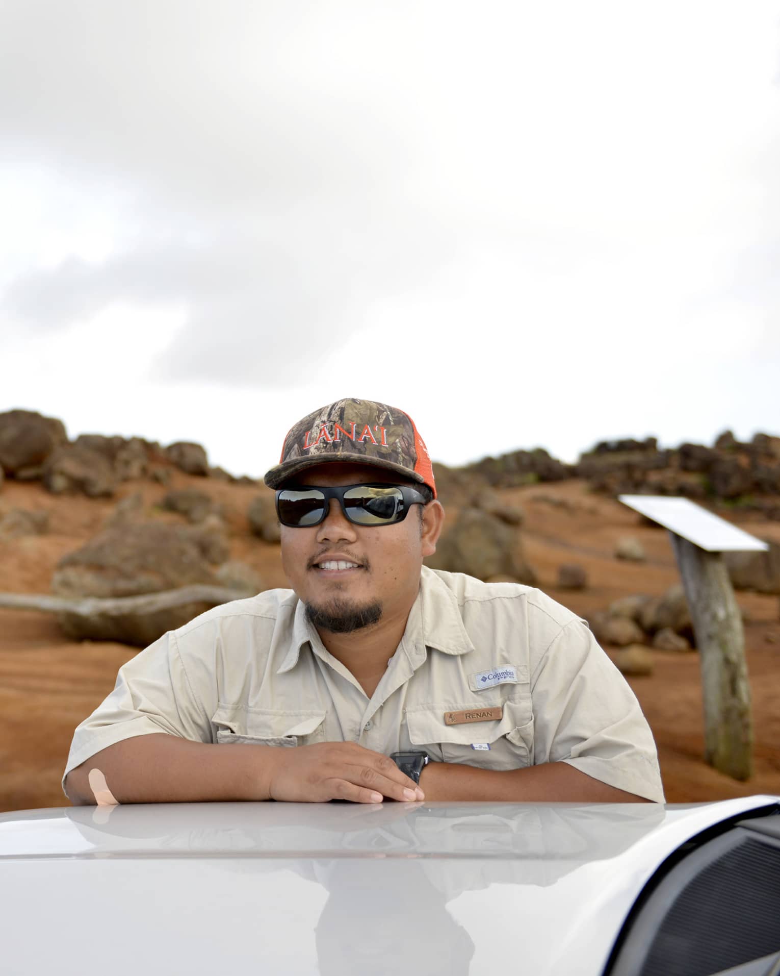 Man leans on top of car, Lanai, Hawaii landscape in the background