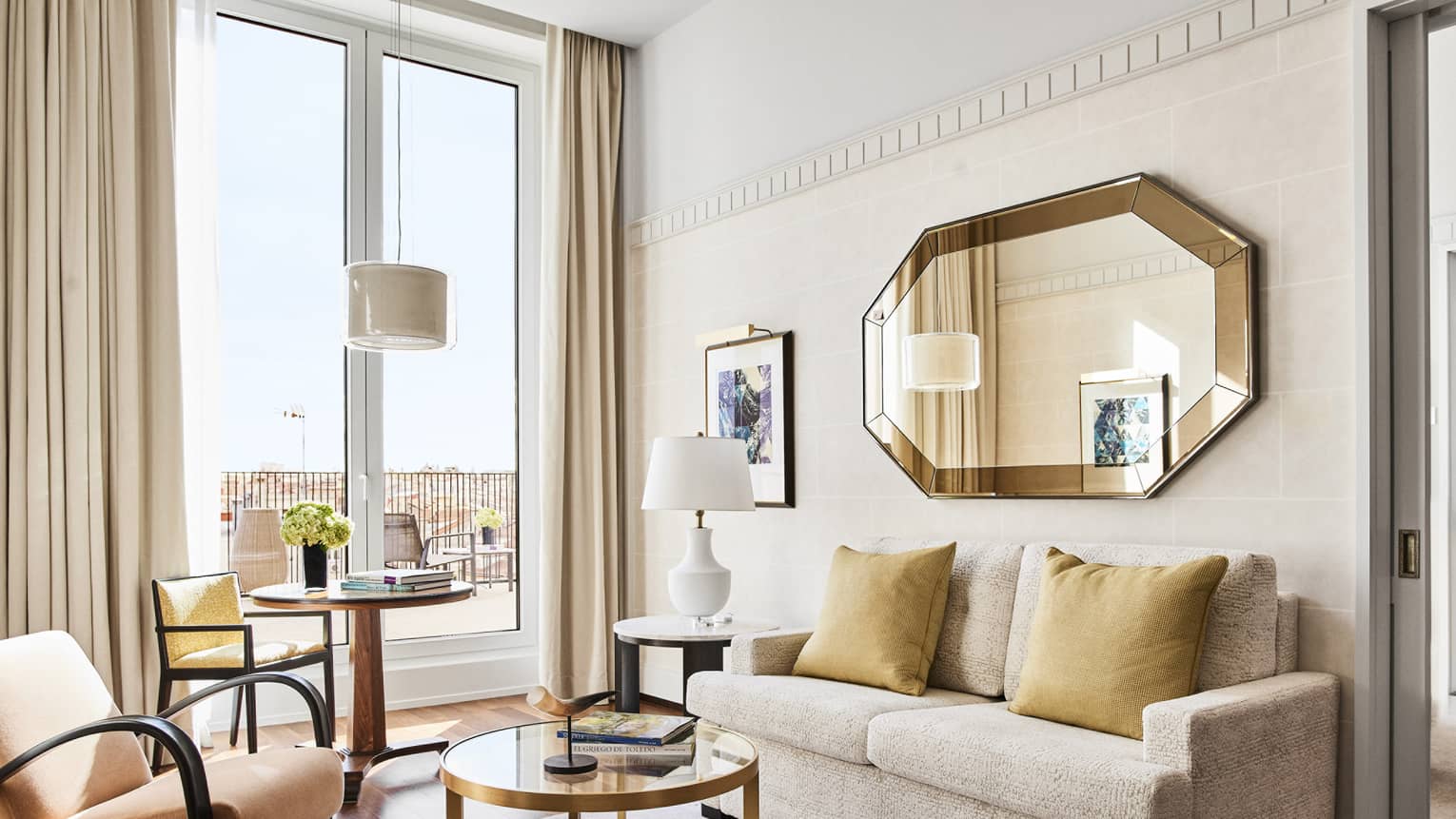 Four Seasons suite living area with a beige sofa, round tables, chairs, octagonal wall mirror and terrace