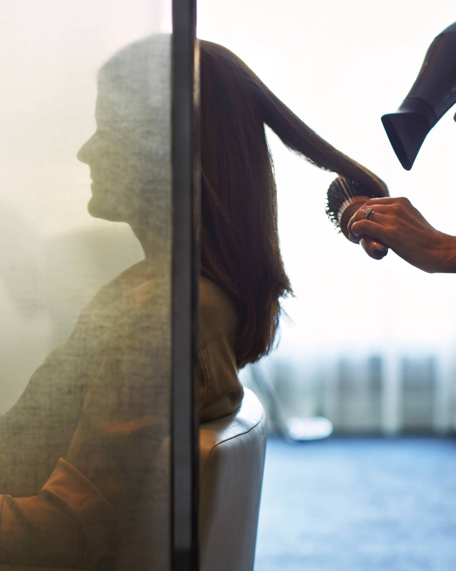 Silhouette of woman behind salon screen as hairdressers brushes, blow dries hair