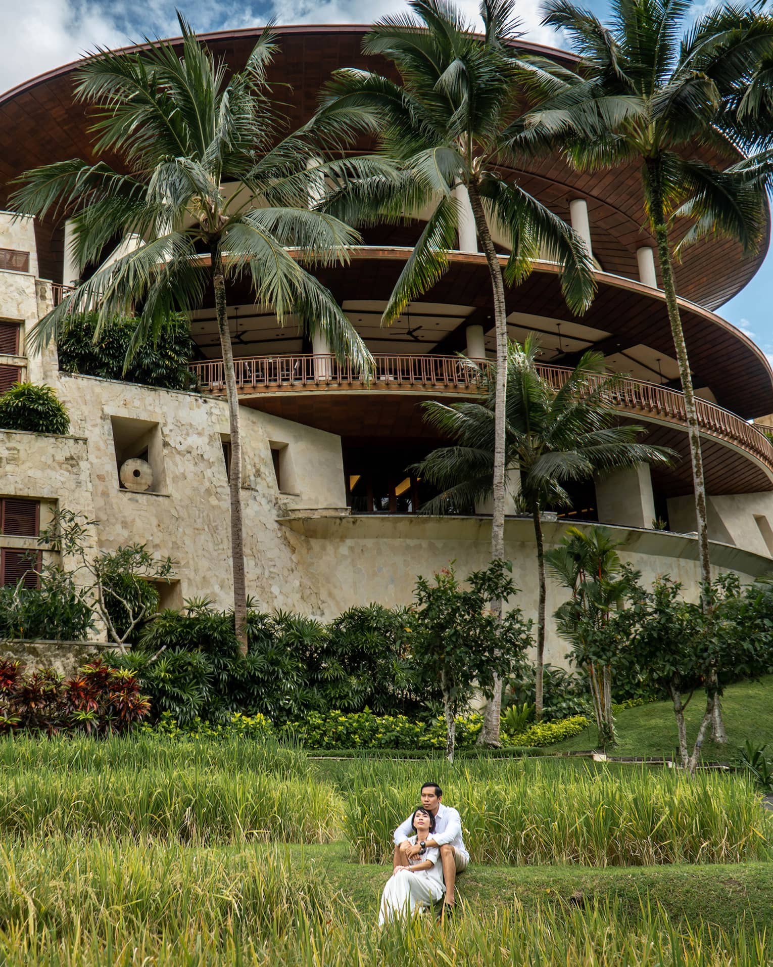 Long view of a couple embracing on the grass in front of the rice-bowl inspired Four Seasons Resort Bali at Sayan.