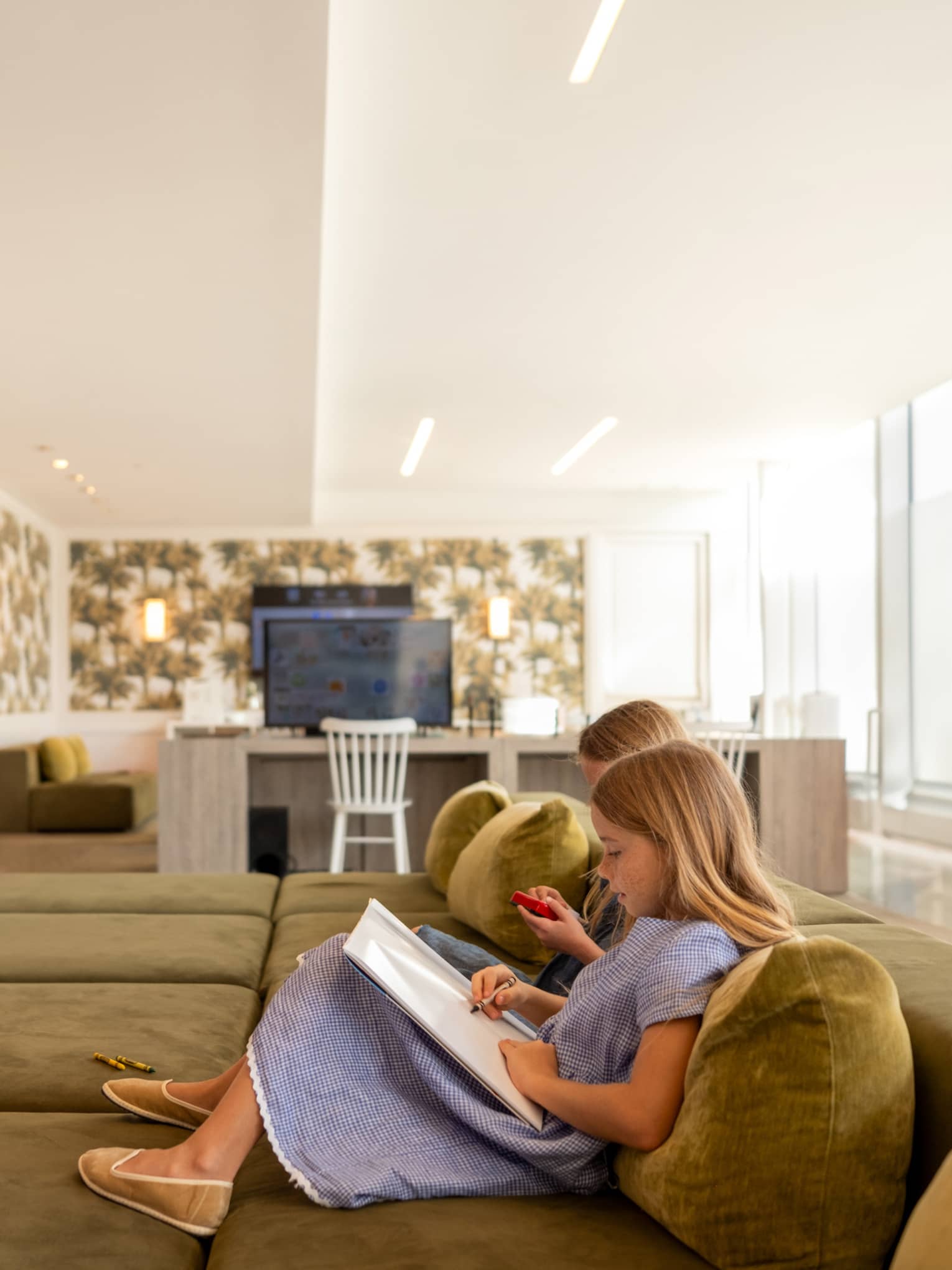 Children watch TV and read books on large sofa in kids club at luxury hotel